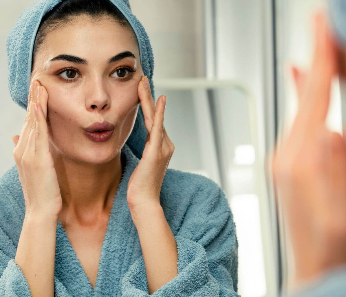 Face Yoga For Women - Woman's Reflection in Bathroom Mirror Practicing Face Yoga Routine 