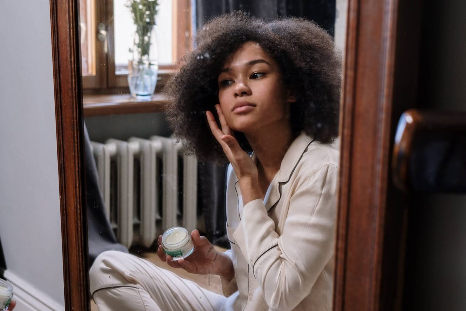 Black Woman in Mirror Applying Face Cream - Black Woman Skincare - Hormonal Skincare For Women
