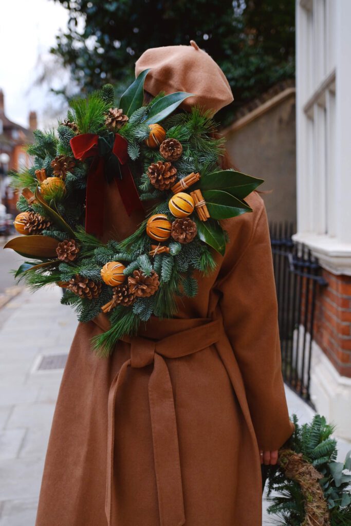 Woman In Hat Carrying Christmas Wreath in London Over Her Shoulder