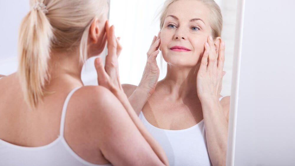 Older woman checking her skin in the mirror, showing how collagen supplements can support skin elasticity and healthy ageing
