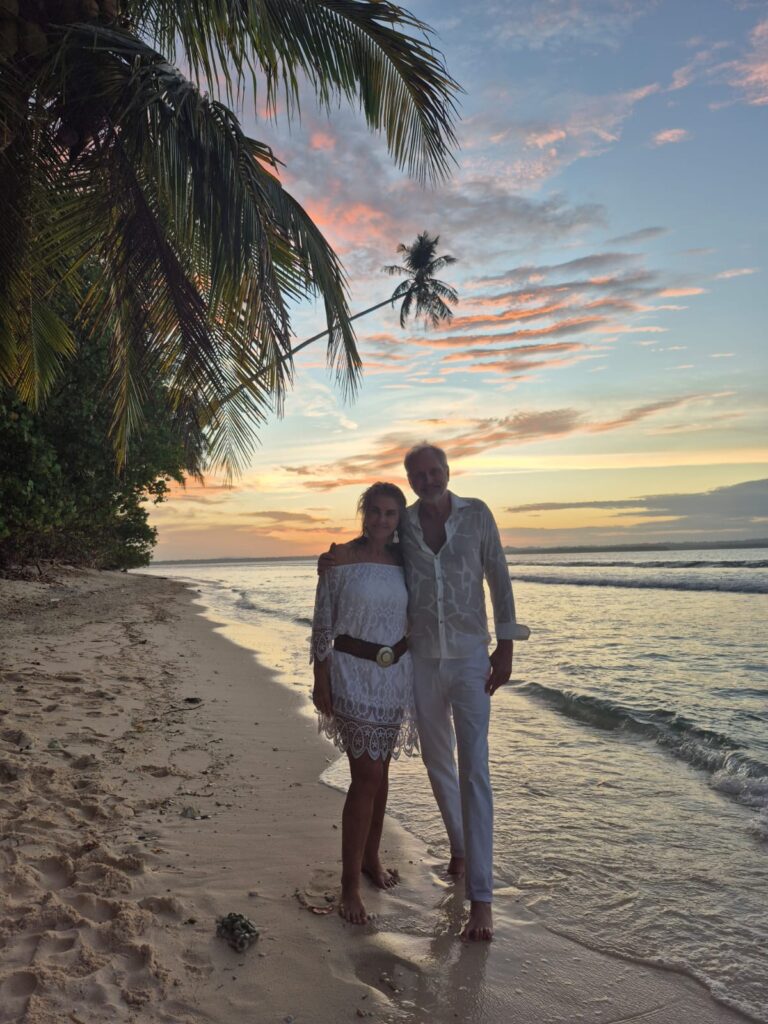 lison Weihe and her husband are travel partners standing on a remote island at sunset, representing their shared love of travel in your 60s