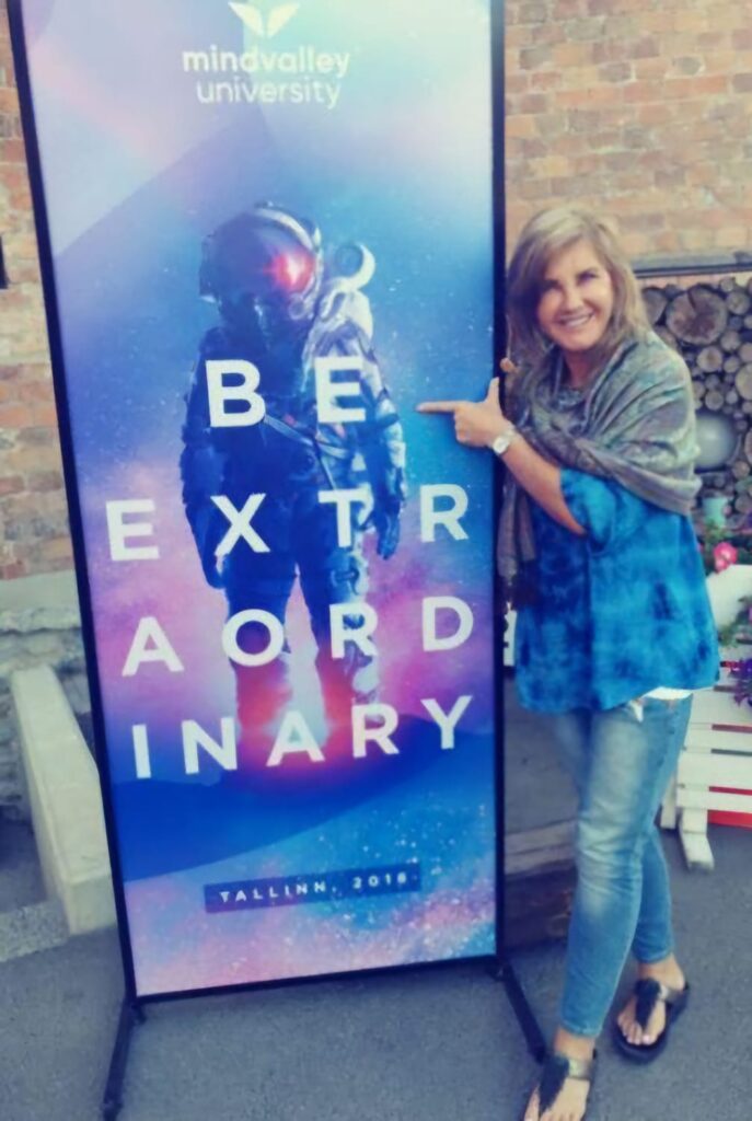 Alison Weihe at Mindvalley University in Tallinn, Estonia, standing next to a poster that reads 'Be Extraordinary' - a moment that inspired her journey