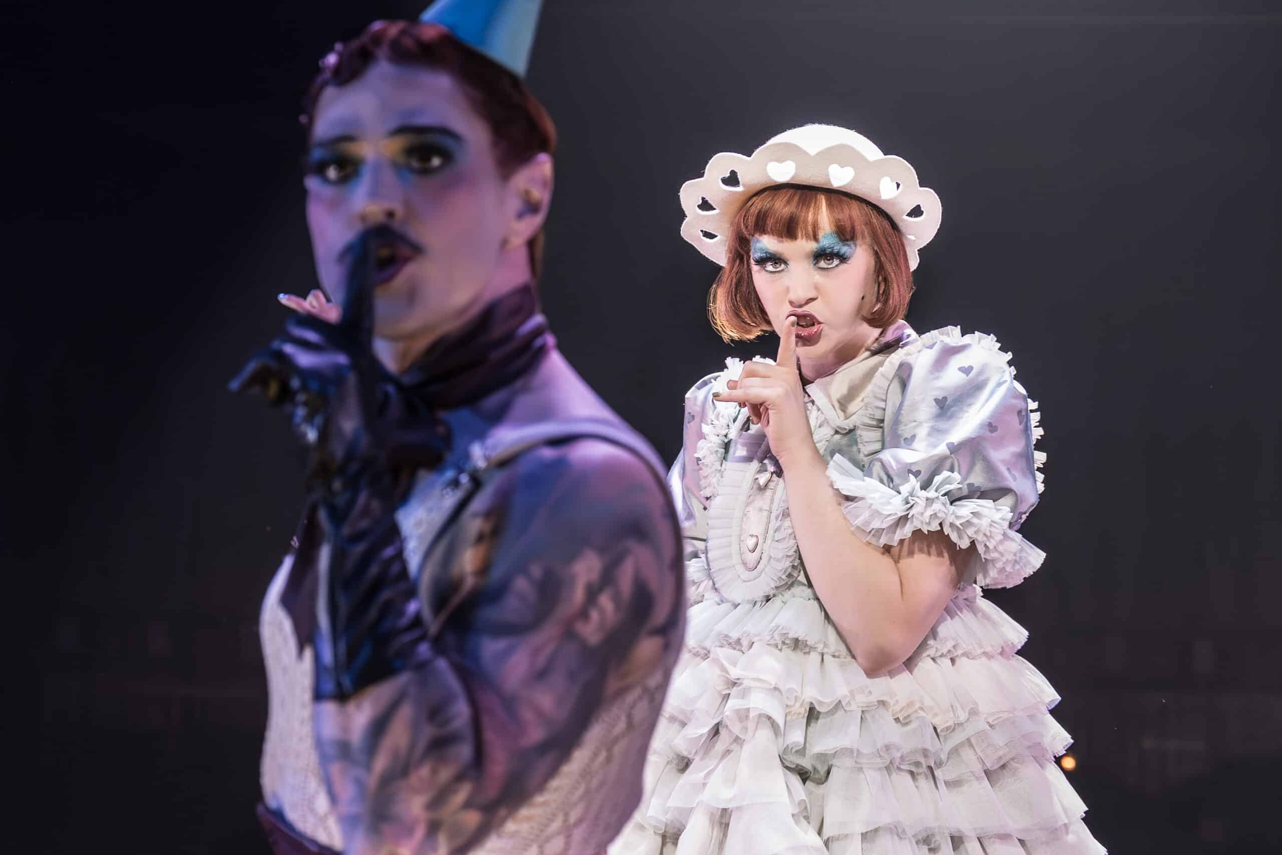Sally Bowles and the master of ceremonies on stage with their fingers in the hush sign at the kit kat club for cabaret