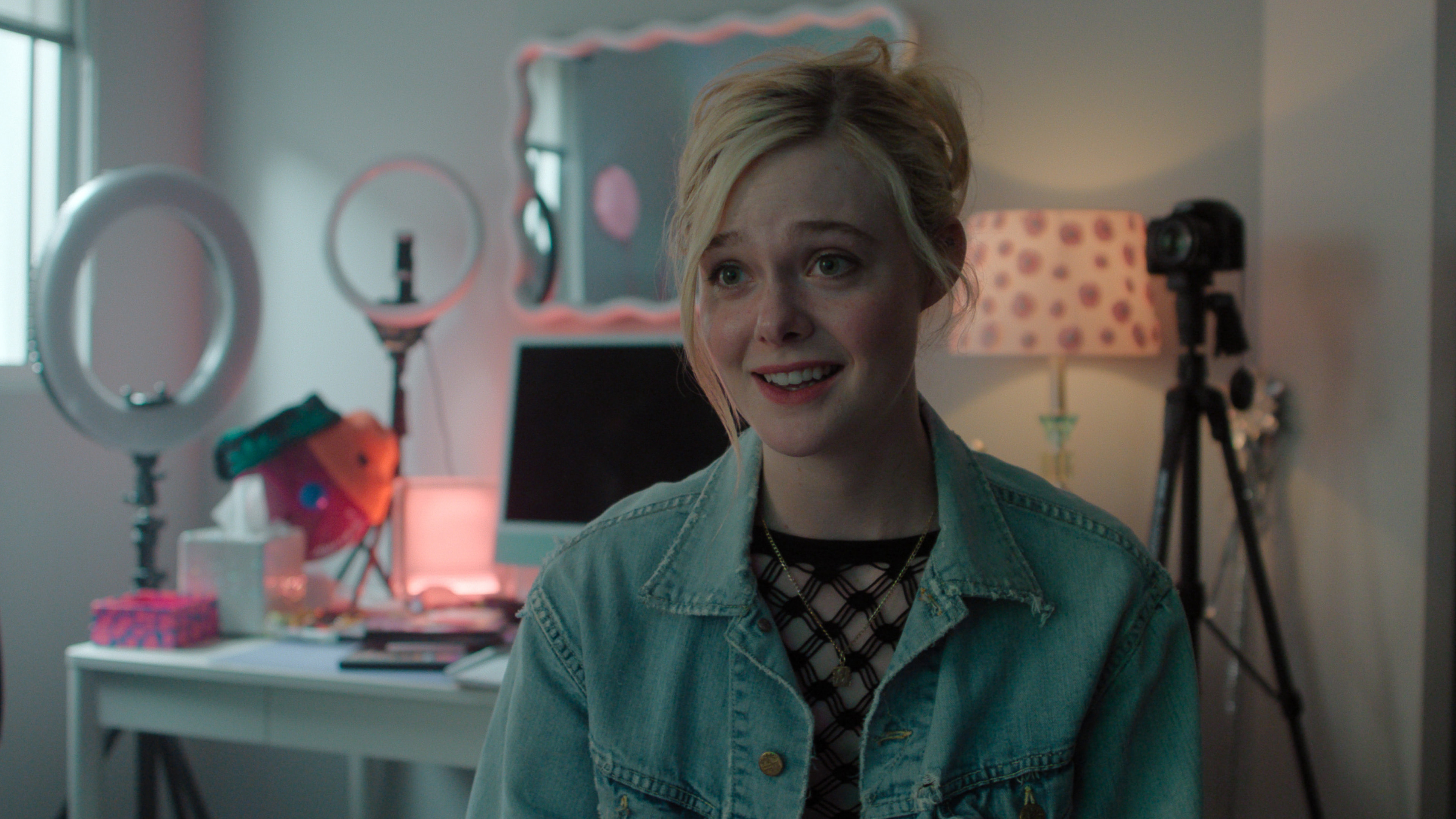Elle Fanning smiling as Margo inside a room filled with tripods and ring lights in 'Margo's Got Money Troubles'.