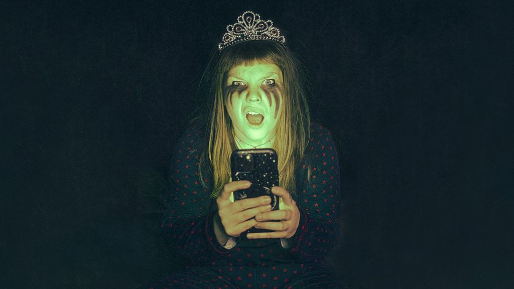 Alfrun Rose wears a tiara and smeared makeup while looking shocked at a glowing phone in new play Dead Air at Greenwich Theatre