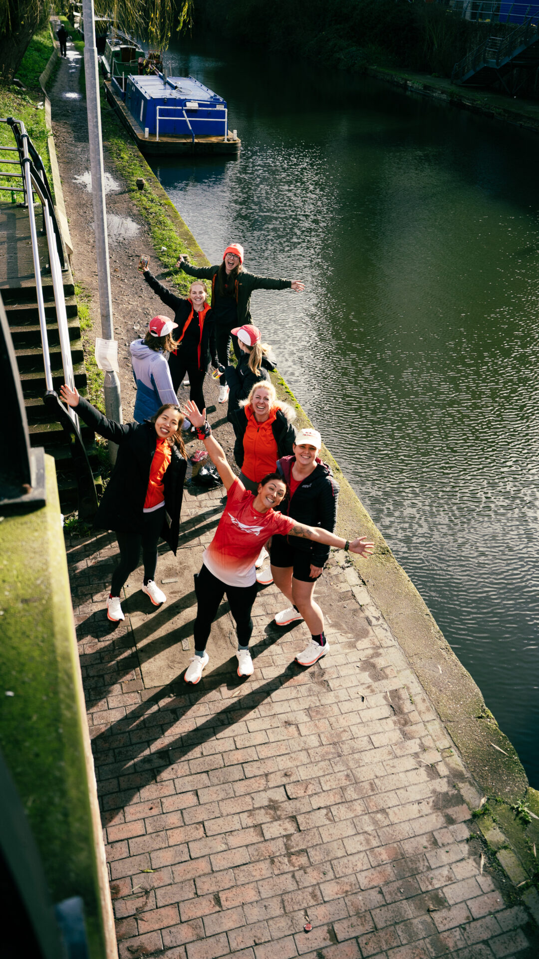 A group of women from the Altra She Runs Free team posing alongside a canal. One woman wears a red top, with her arms outstretched, posing for the photograph