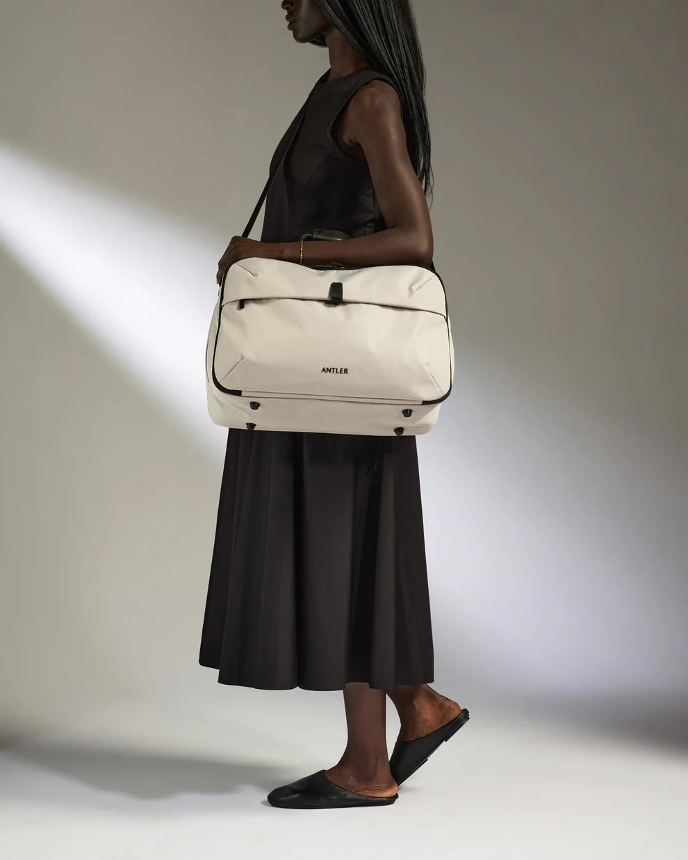 Model holding Antler Overnight Bag in taupe, a light coloured bag with black handles and a front pocket