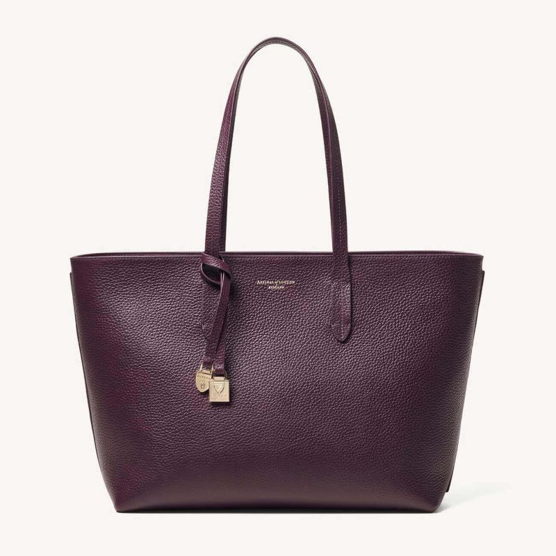 Aspinal of London zipped East West tote bag in fig pebble leather with gold shield charm and long shoulder straps.