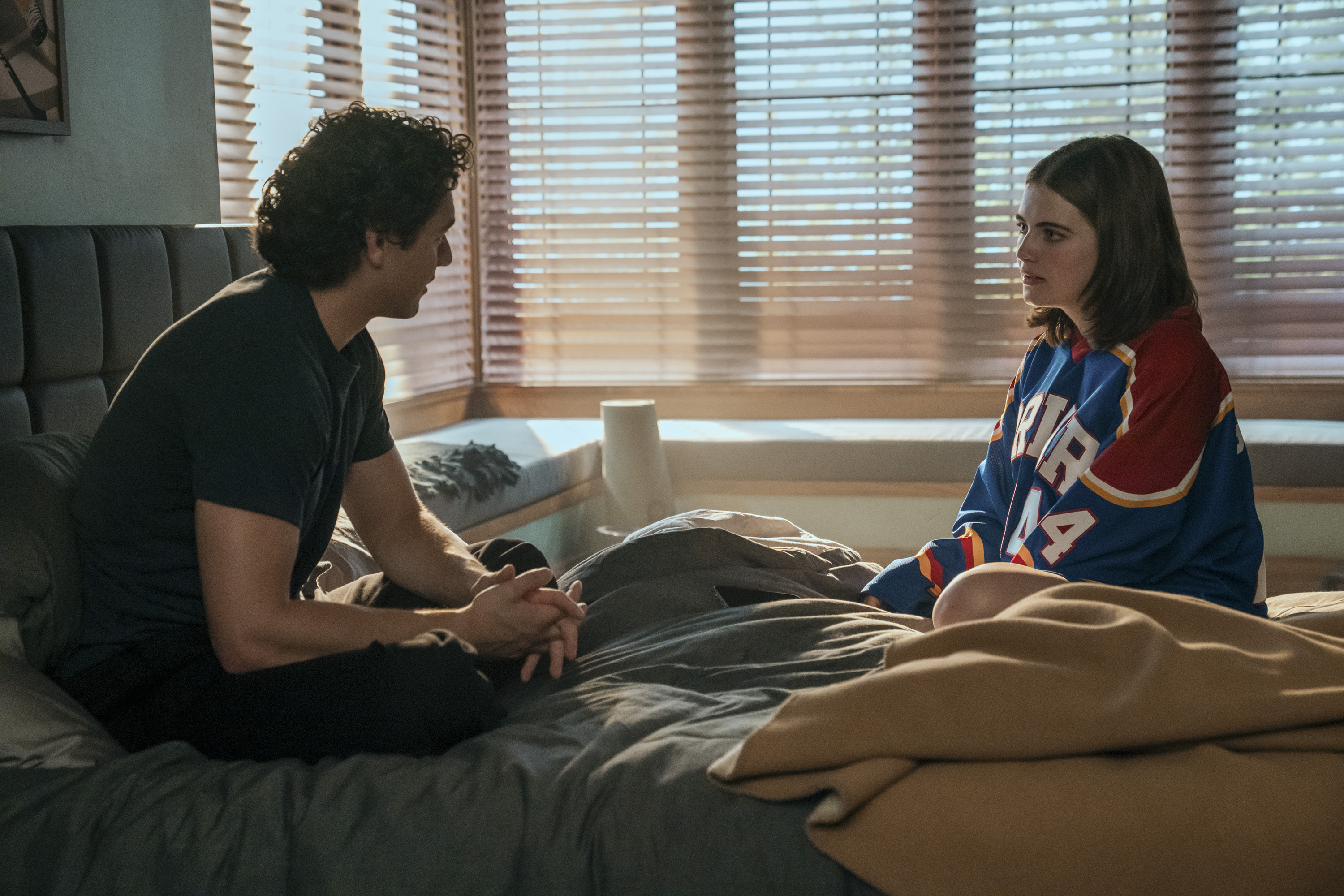 Belmont Cameli as Garrett and Ella Bright as Hannah sitting across from each other in bed in a scene from 'Off Campus'.