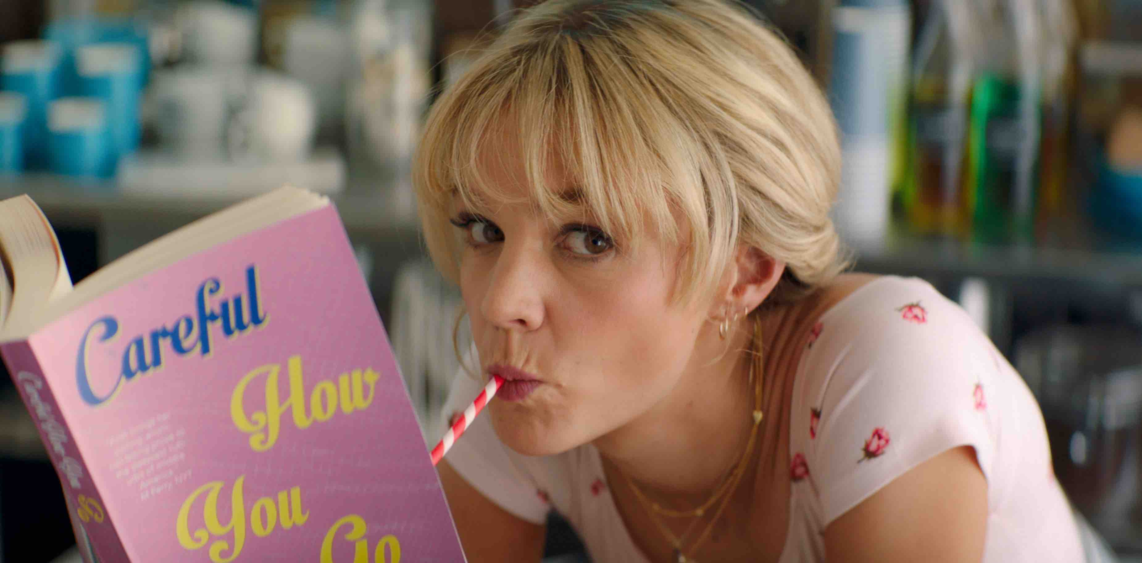 Carey Mulligan as Cassie, sipping out of a straw while reading a book in a scene from 'Promising Young Woman'.