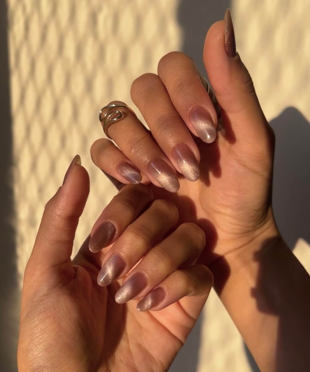 Almond-shaped nails with a soft champagne chrome finish on a glossy nude base, creating a subtle shimmer spring manicure