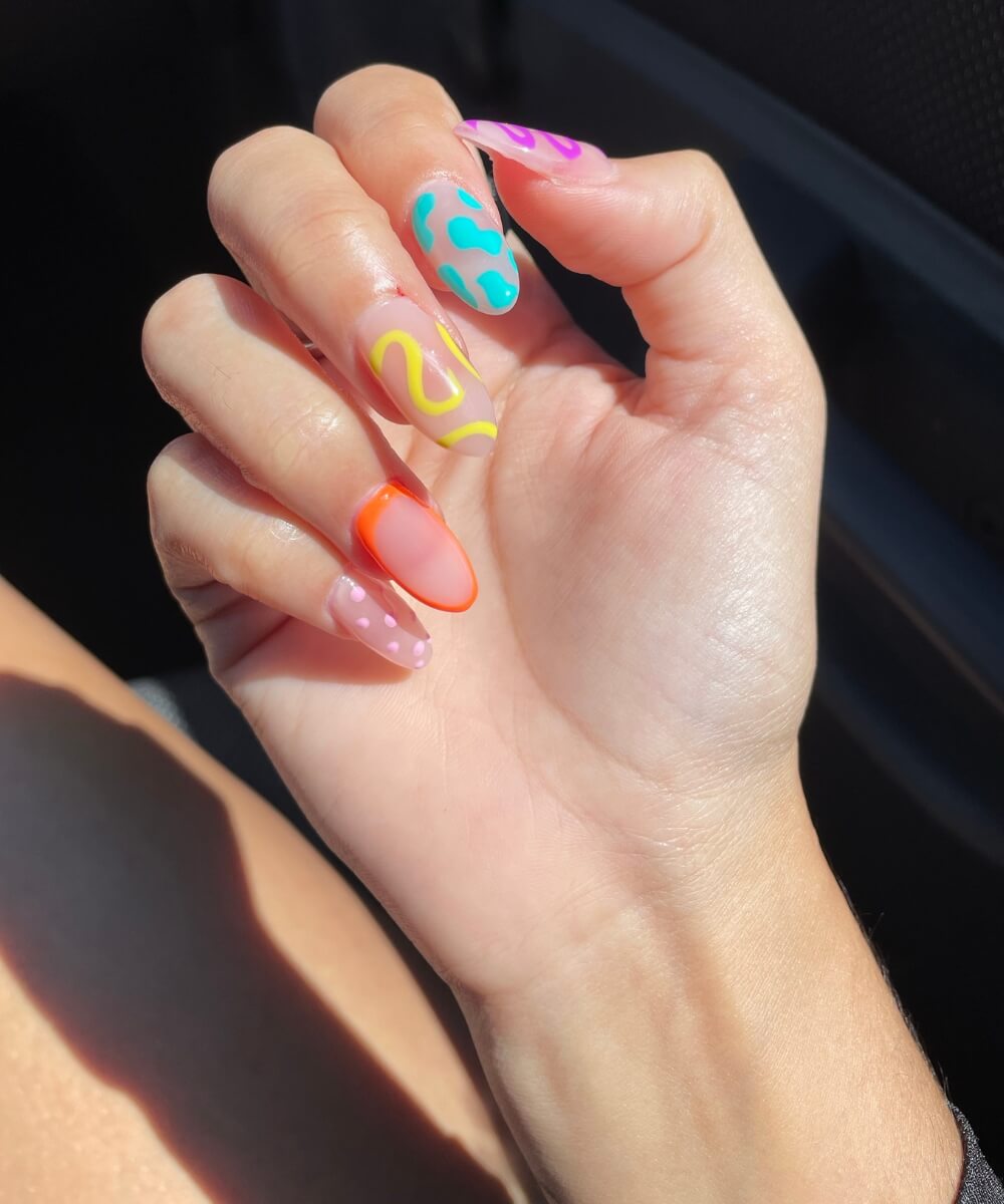 Almond-shaped spring nails with colourful mix-and-match designs including abstract swirls, animal print and neon French tips on a glossy nude base
