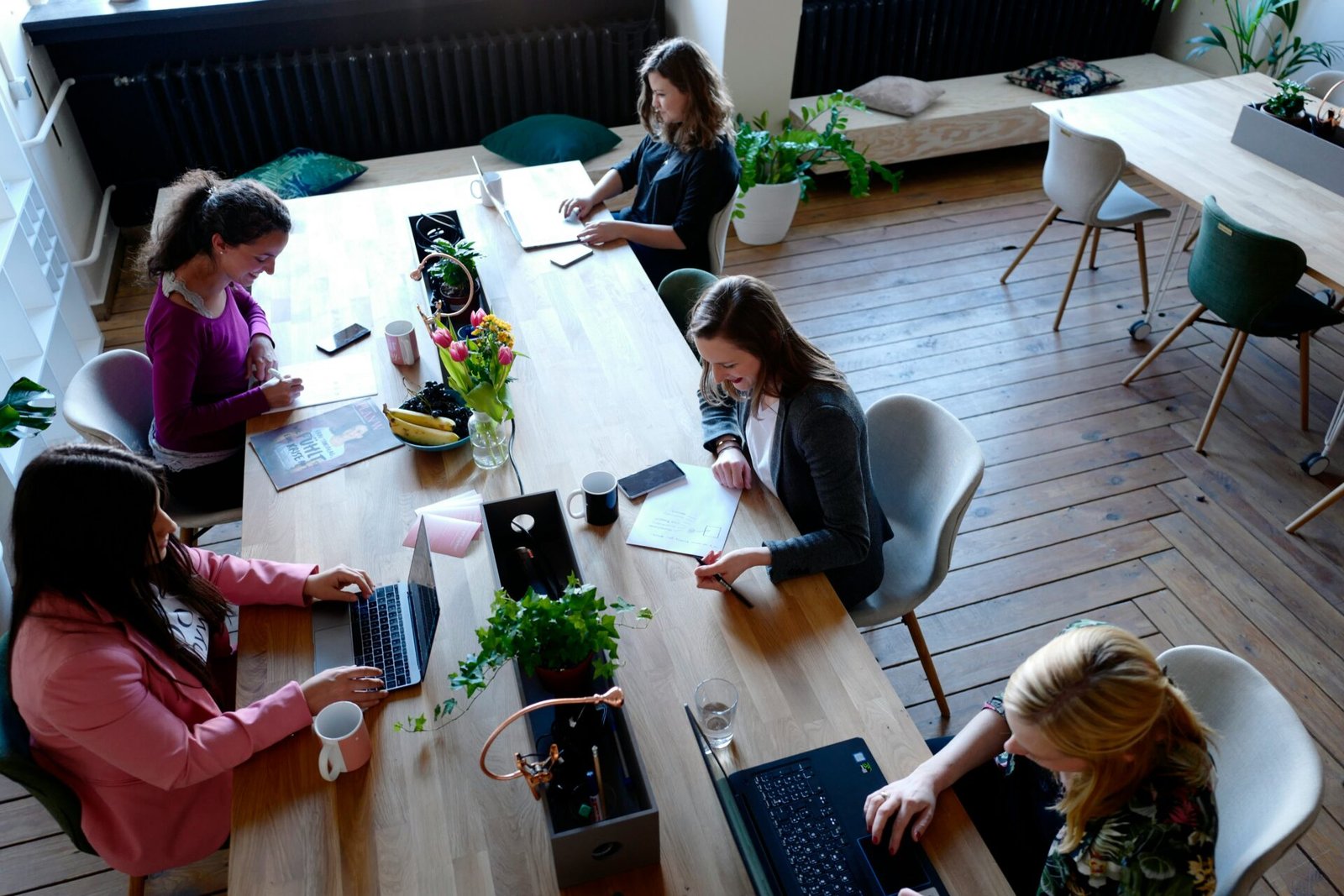 A group of five female founders seated at a table, each using laptops and engaged in discussion - best investors for female founders