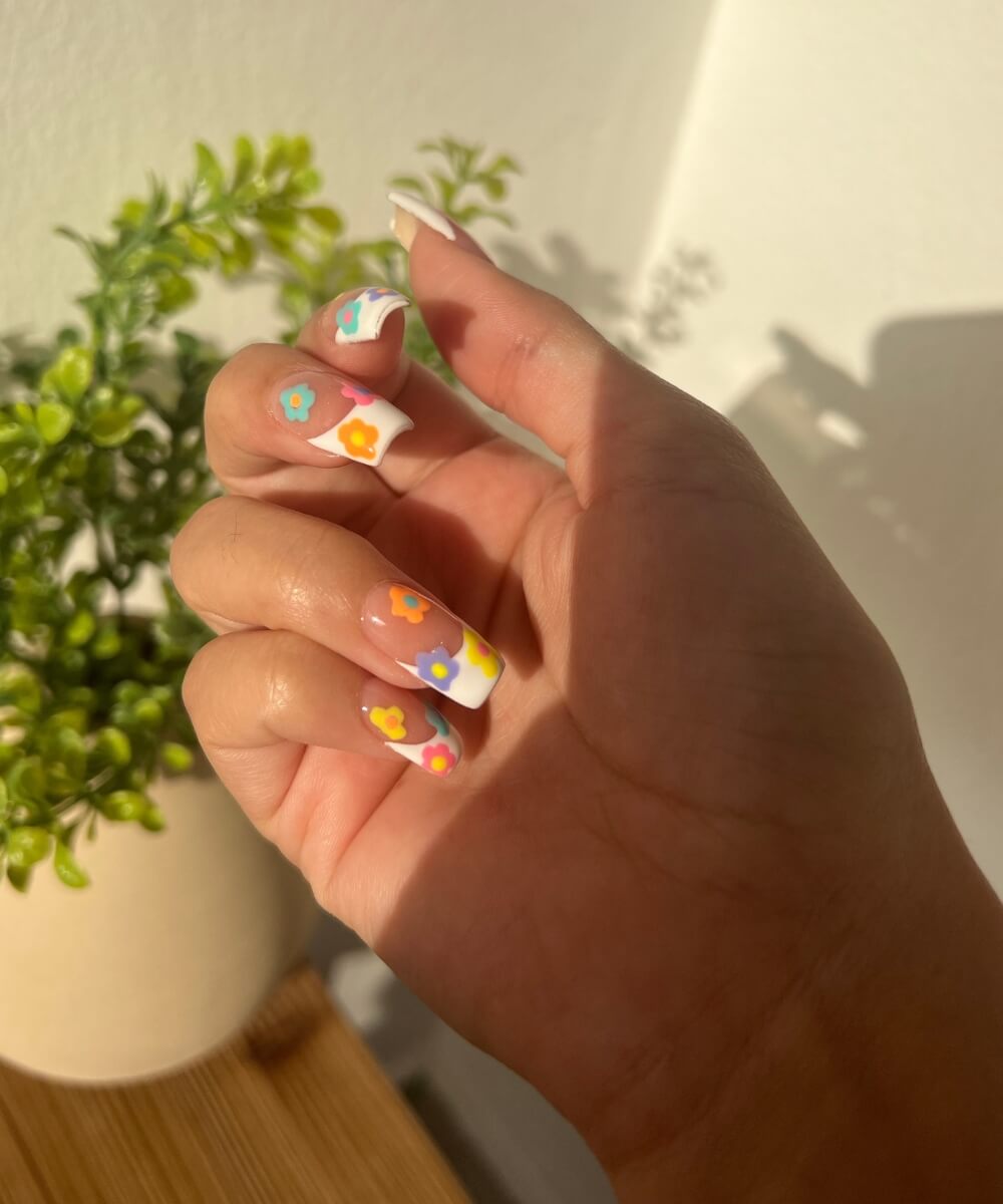 Spring nail art with colourful floral designs and pastel French tips on glossy nude nails, featuring daisy patterns in soft and bright shades
