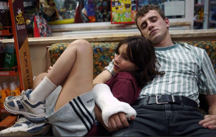 Frankie Corio as Sophie lying on Paul Mescal's lap as his character Calum falls asleep and wraps his right arm with a cast around her in a scene from 'Aftersun'.