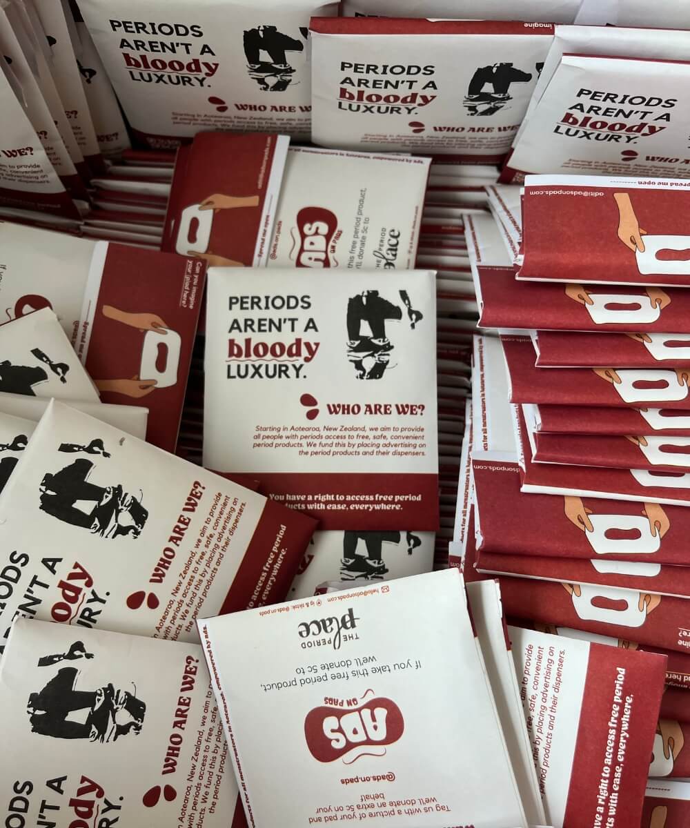 Stacks of packaged period products with messaging that reads 'Periods aren’t a bloody luxury' highlighting awareness of period poverty and access to free period products