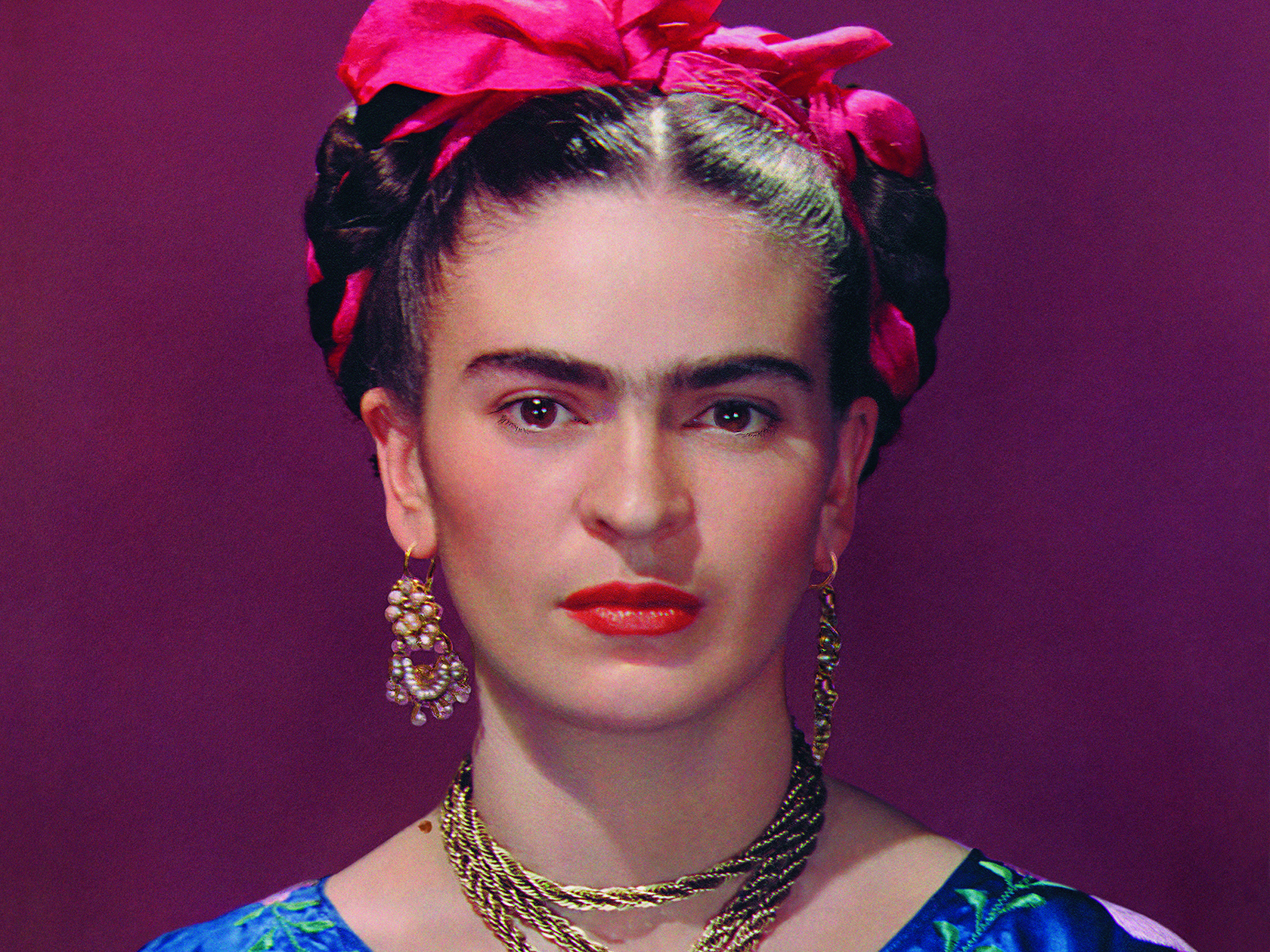 Detailed portrait of Frida Kahlo with braided hair, a bright pink head ribbon, and ornate gold jewelry against a dark red background.