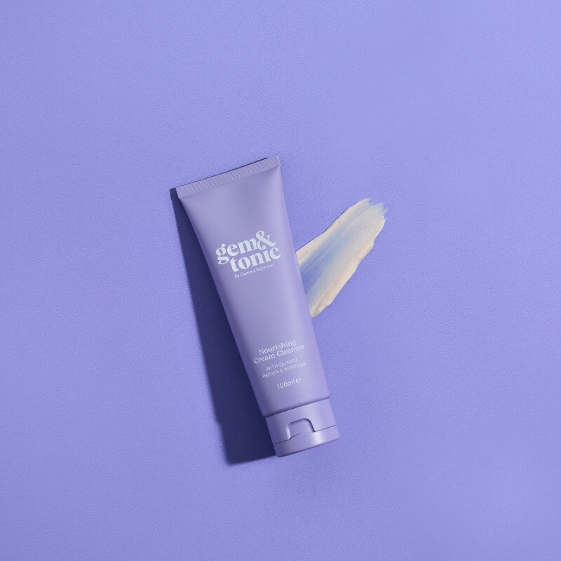 A purple tube of Gem & Tonic Nourishing Cream Cleanser with a cream swatch beside it on a matching background