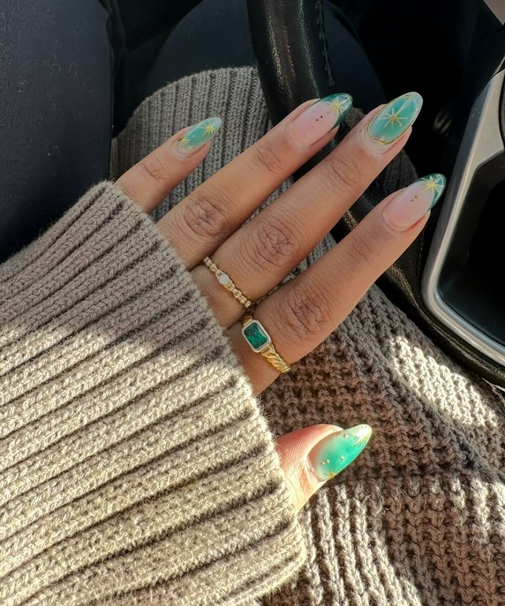 Close-up of almond-shaped nails with green ombré tips and delicate star nail art on a glossy nude base, creating a soft spring manicure