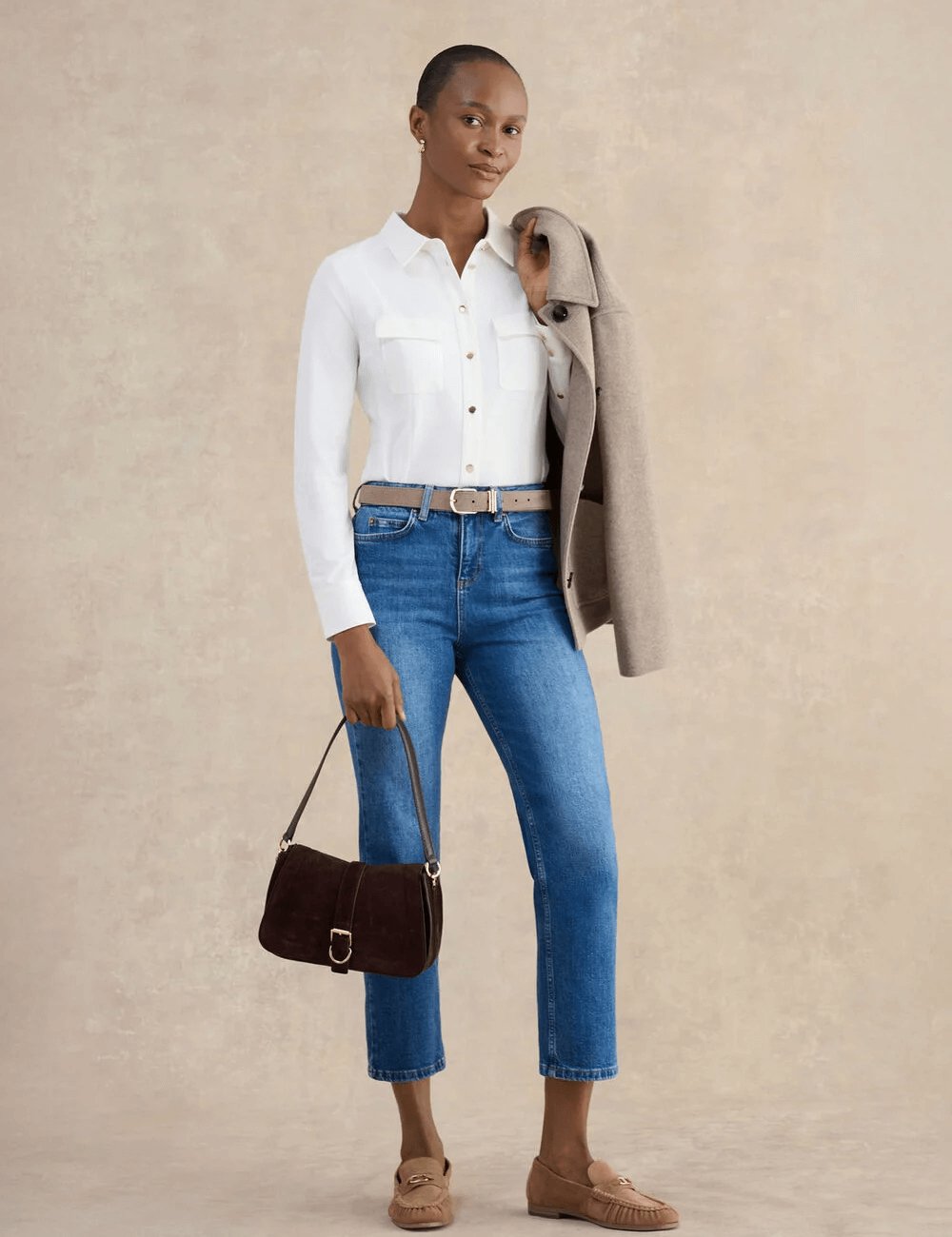 Model wearing Hobbs Rosana seamed shirt in ivory styled with blue jeans, beige belt, loafers and a shoulder bag