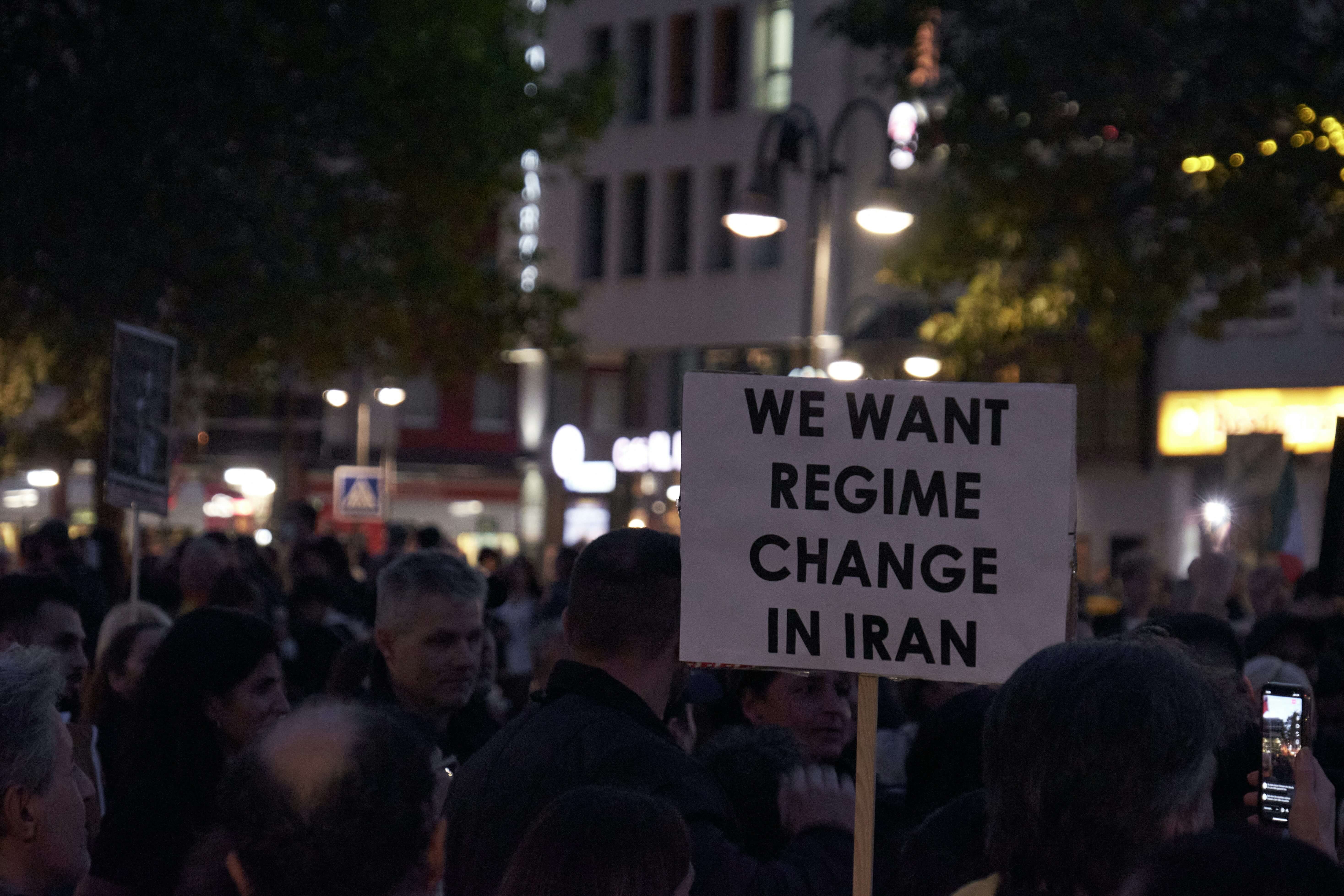 Protesters holding a sign reading 'We want regime change in Iran' during a night-time demonstration
