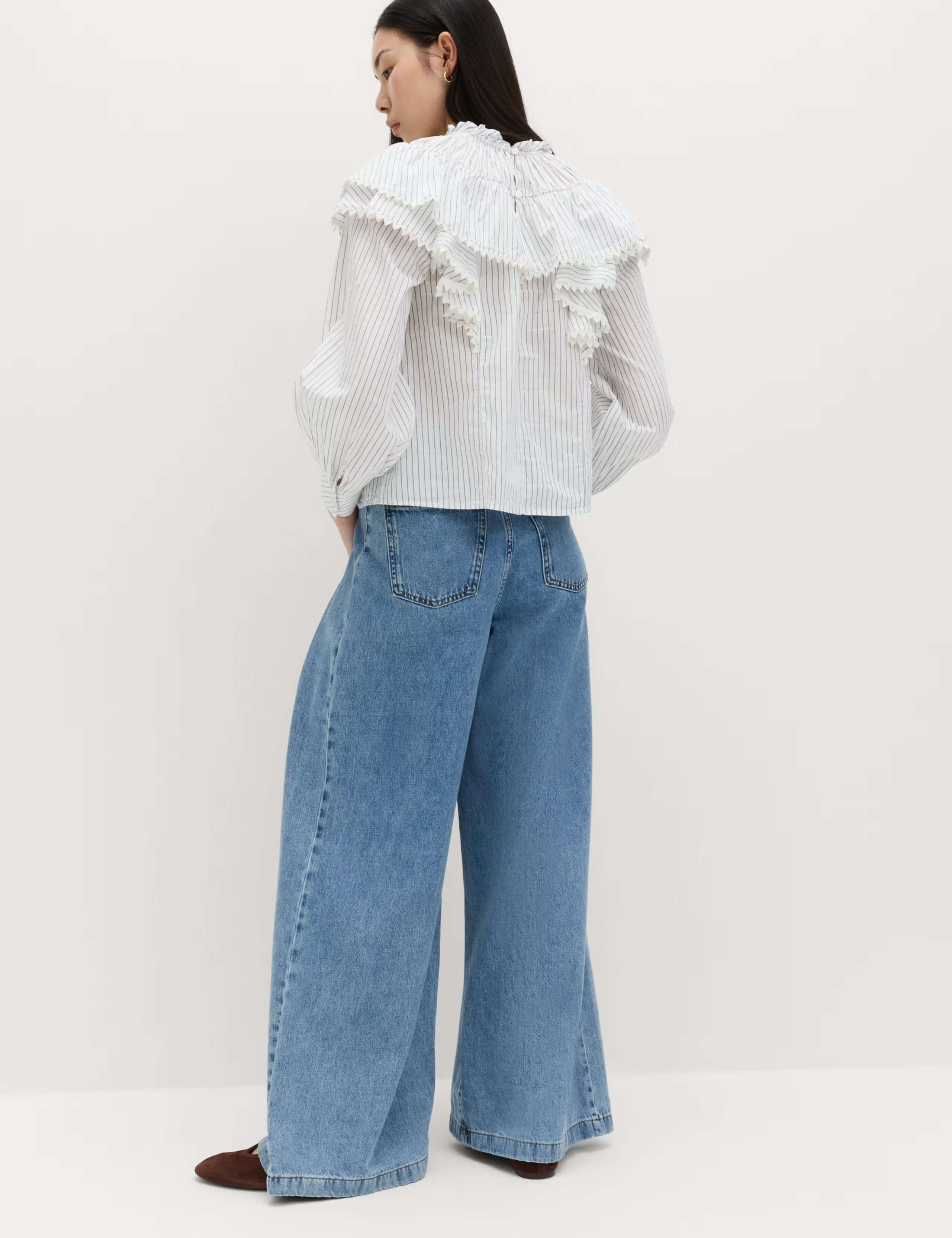 Back view of Model wearing M&S pure cotton striped lace detail blouse, a white long-sleeve blouse with vertical stripes, featuring a large, ruffled collar and cuffs