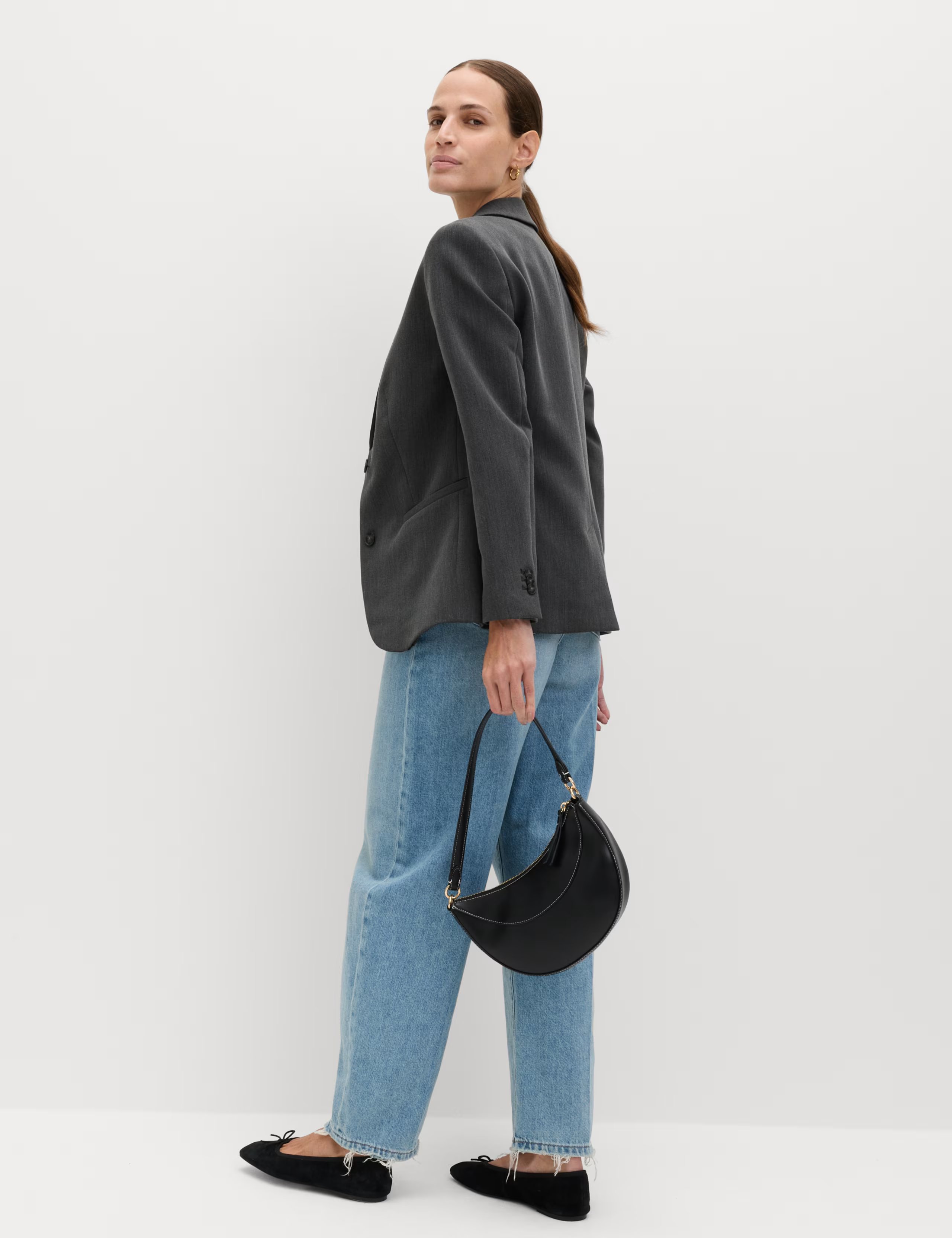 Model wearing M&S Relaxed Tailored Single-Breasted Blazer in grey colour, a smart option for women's workwear, holding a black handbag and wearing blue jeans