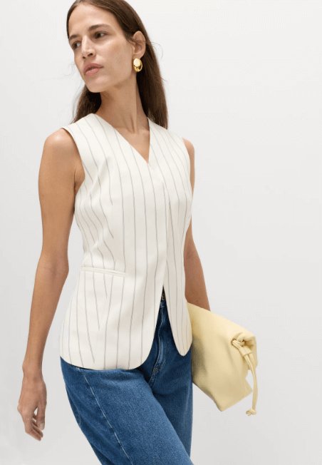 Model wearing M&S Striped V-Neck Longline Waistcoat, an ivory pinstriped sleeveless white waistcoat with blue jeans and a beige clutch