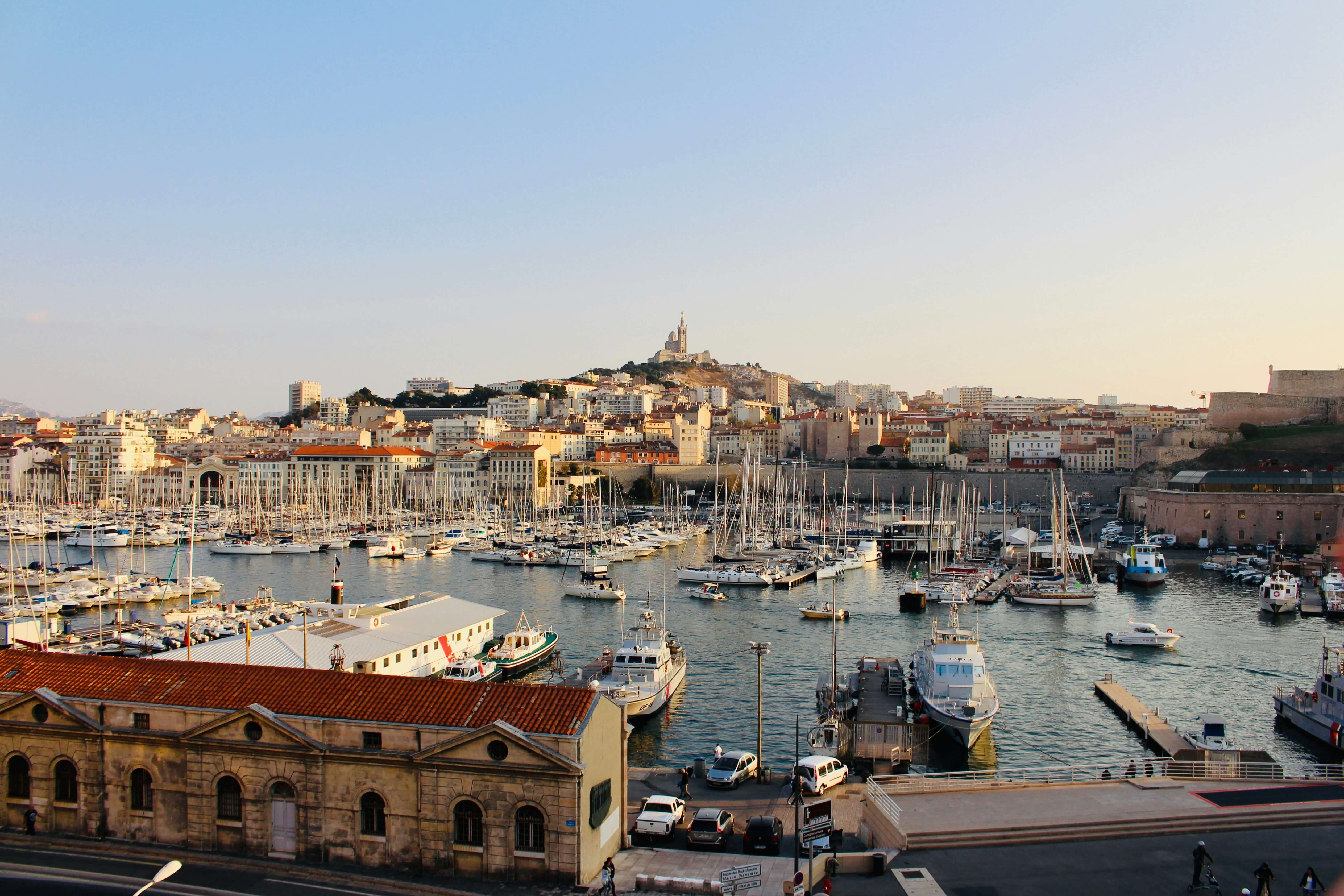 Boats docked in Marseille’s Old Port with the city skyline and Notre-Dame de la Garde basilica on a hill at sunset