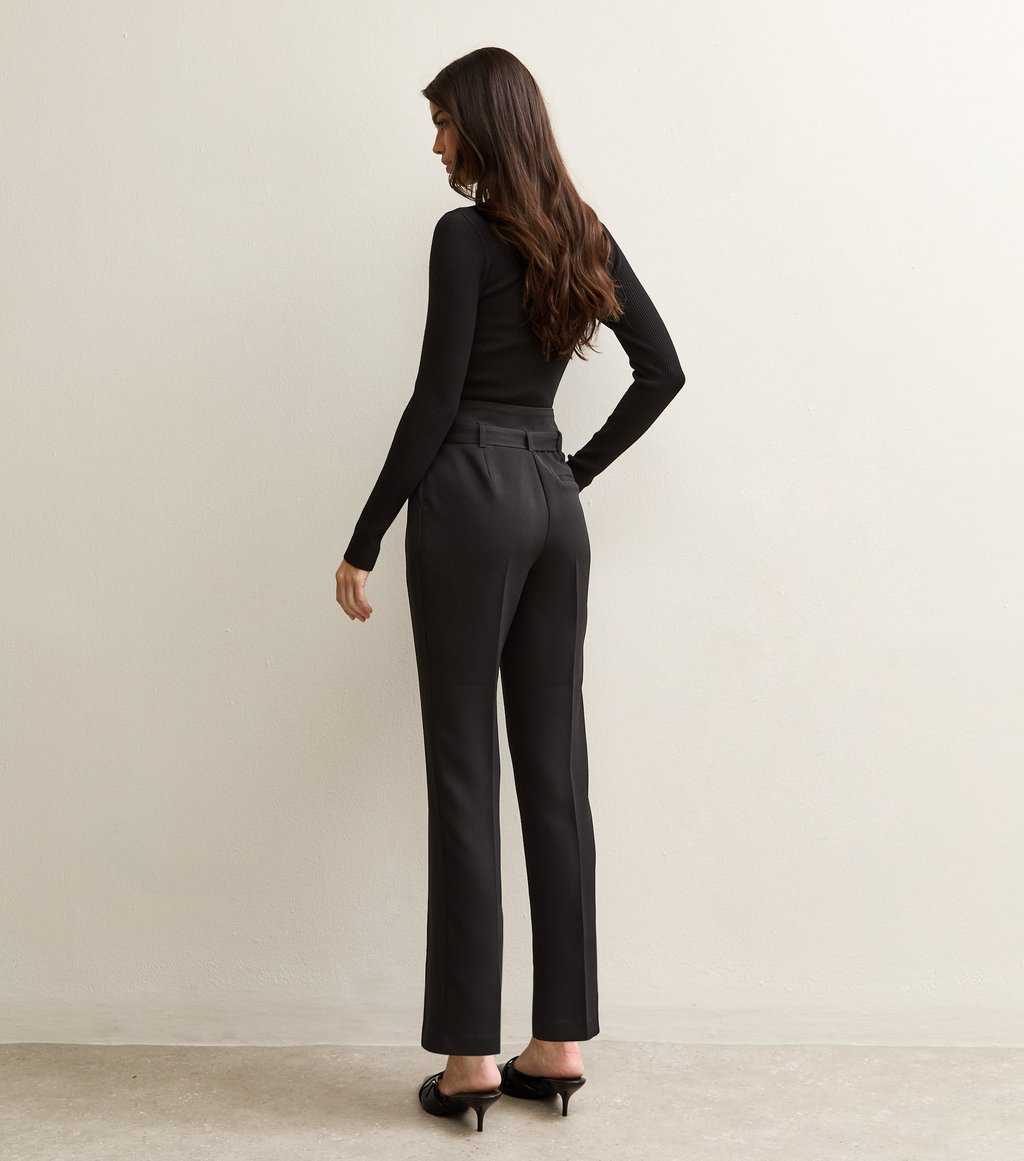 Model wearing New Look black belted paperbag waist trousers, paired with a black turtleneck and heels, back view