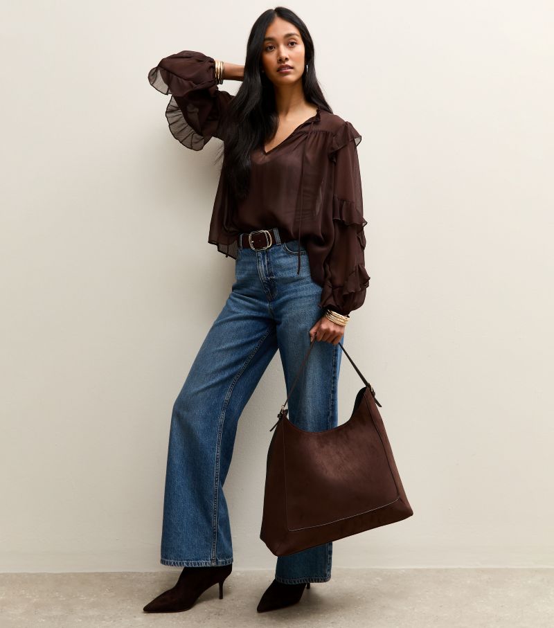 Woman carrying New Look dark brown faux suede scoop top tote bag styled with jeans and blouse.
