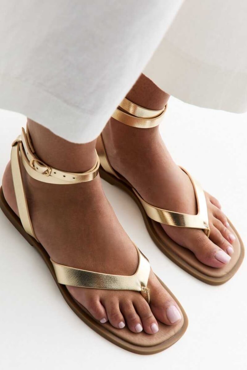 New Look gold ankle strap sandals with a toe post design worn on bare feet