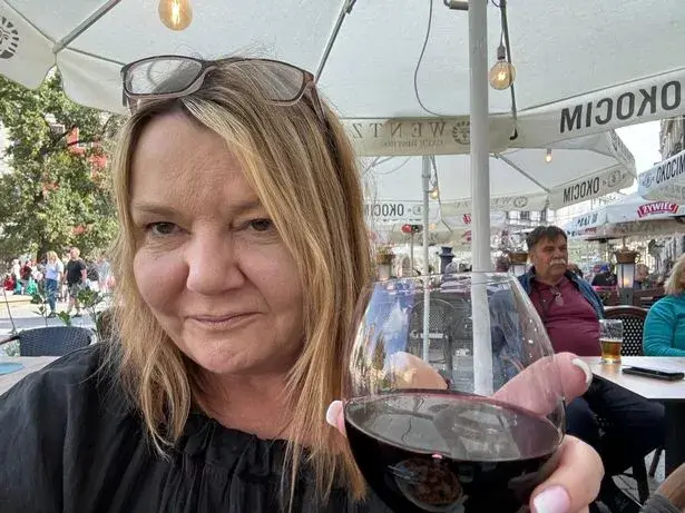 Nicky Wake wearing a black blouse sitting at an outdoor café table holding a glass of red wine before choosing midlife sobriety