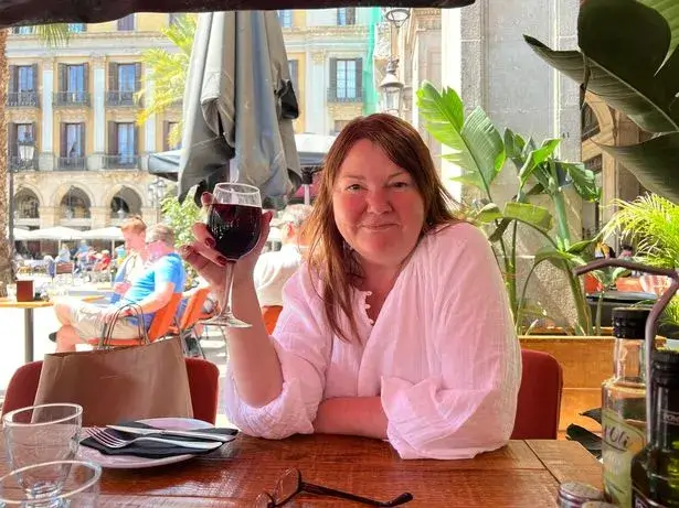 Nicky Wake wearing a white blouse sitting at an outdoor restaurant table holding a glass of red wine before quitting alcohol