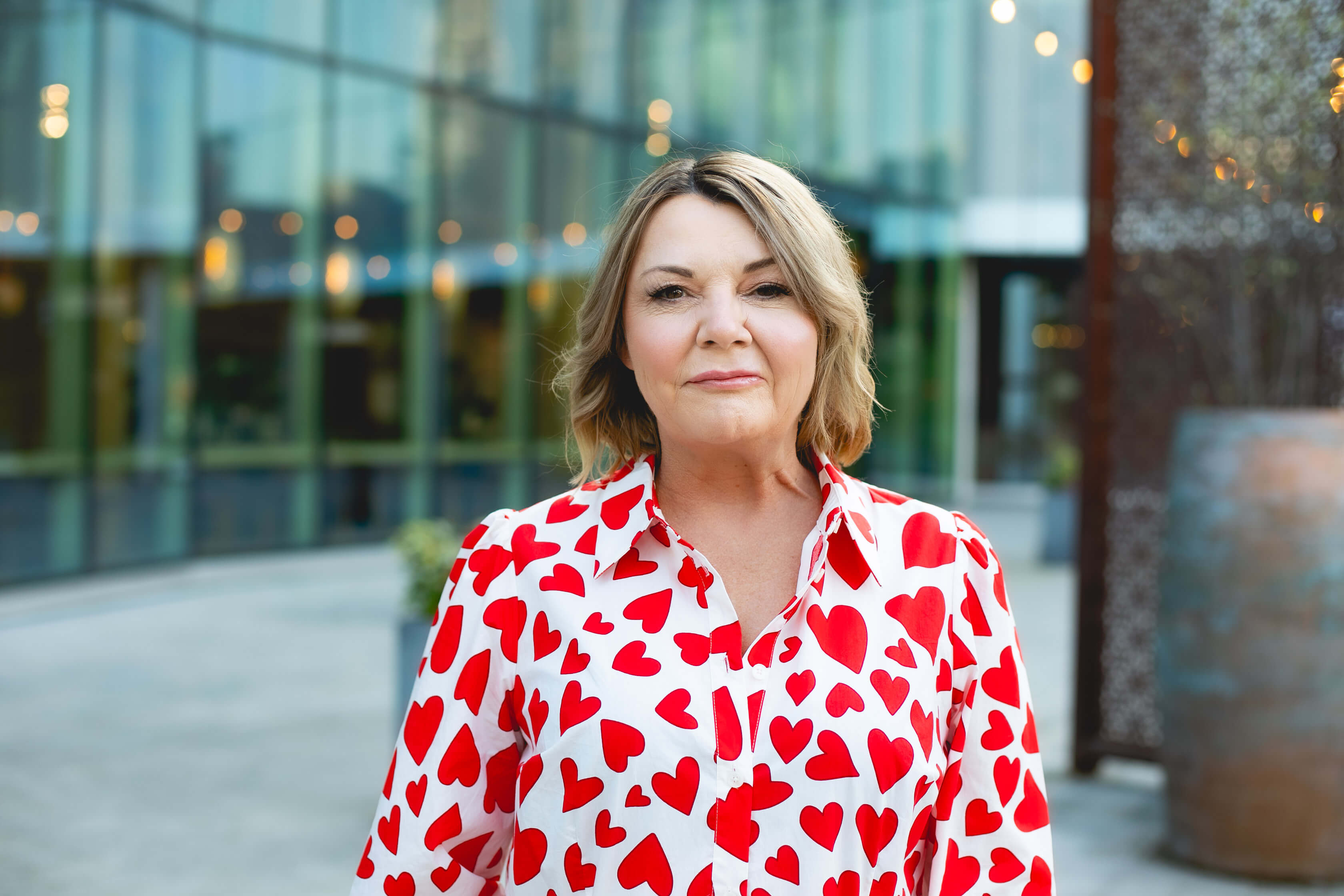Nicky Wake, founder of Sober Rebel Society, wearing a white blouse with red heart prints standing outdoors as an advocate for midlife sobriety