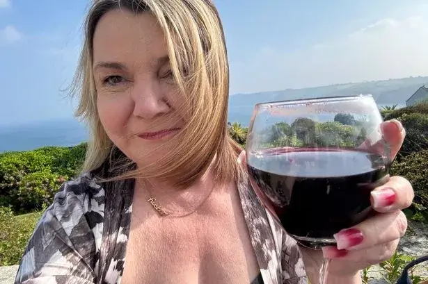 Nicky Wake wearing a patterned blouse outdoors by the sea holding a large glass of red wine during the years she describes as functioning alcoholism