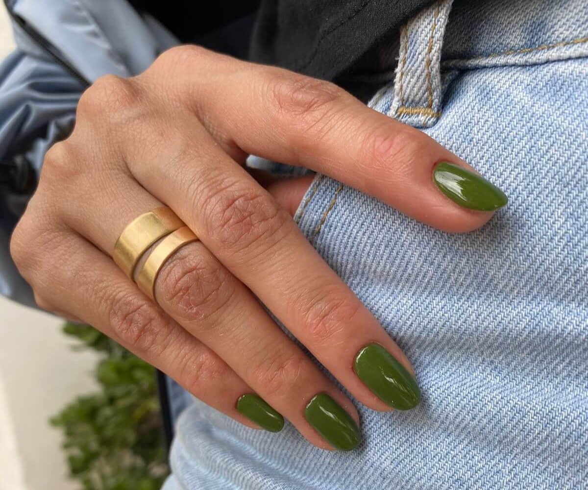Olive green almond-shaped spring nails with a glossy finish, styled with gold rings and casual denim - spring nail ideas 2026