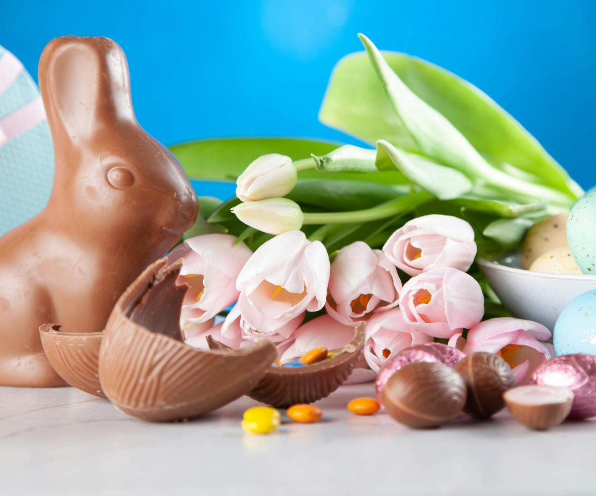 Palm oil-free chocolate Easter bunny and broken palm oil-free chocolate eggs with pastel Easter eggs and spring tulips - round-up of the best palm oil-free easter eggs for easter 2026