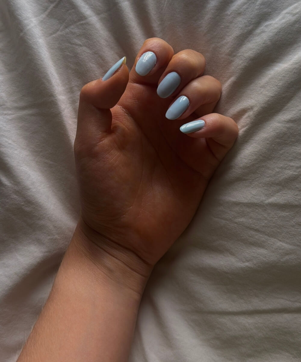 Close-up of glossy pastel blue nails on short oval-shaped nails, featuring a smooth, minimal spring manicure