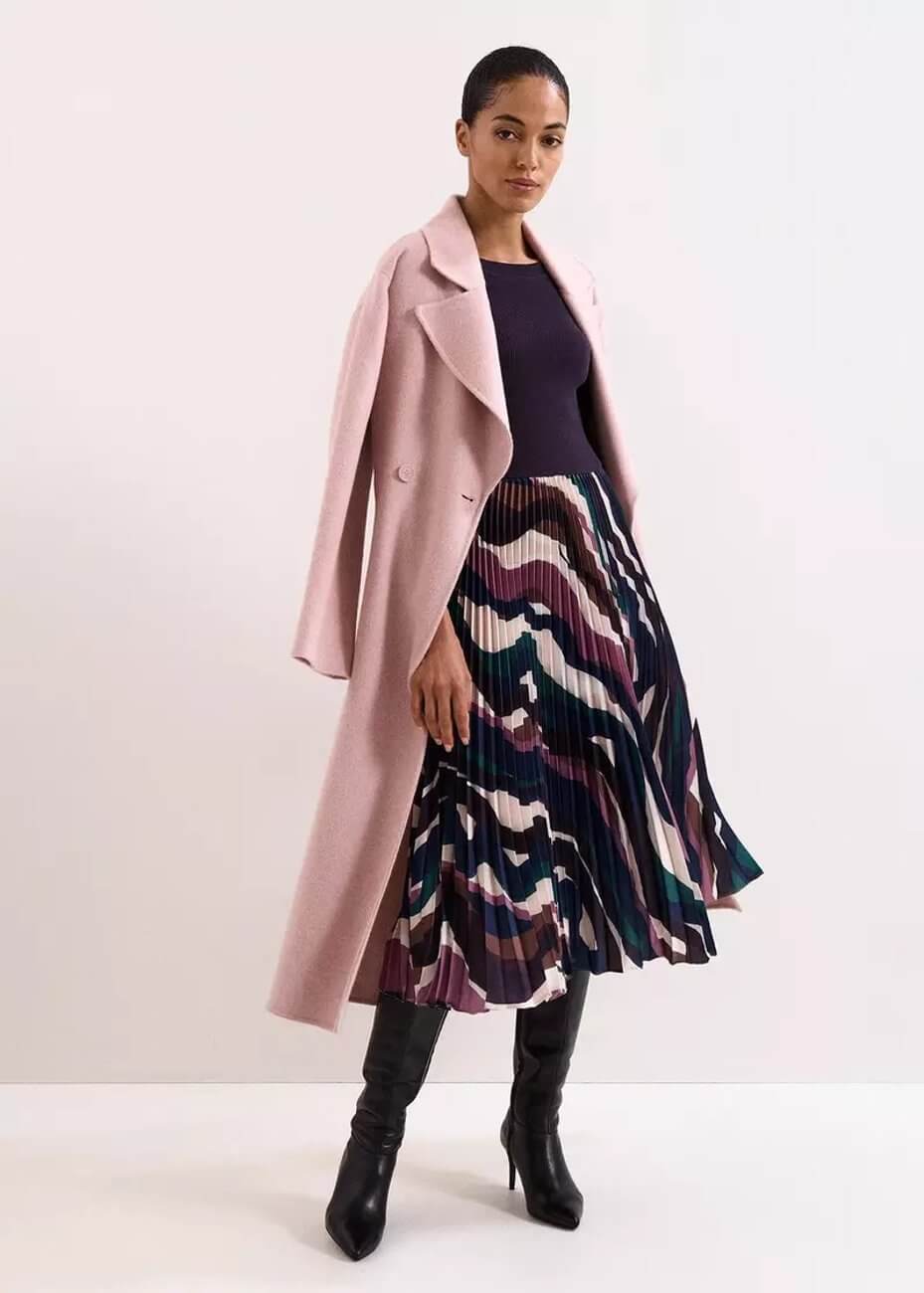 Model wearing Phase Eight Riley Woven Dress, a pleated dress featuring a purple fitted bodice and a colourful abstract pattern on the skirt, paired with a pink coat and black heels