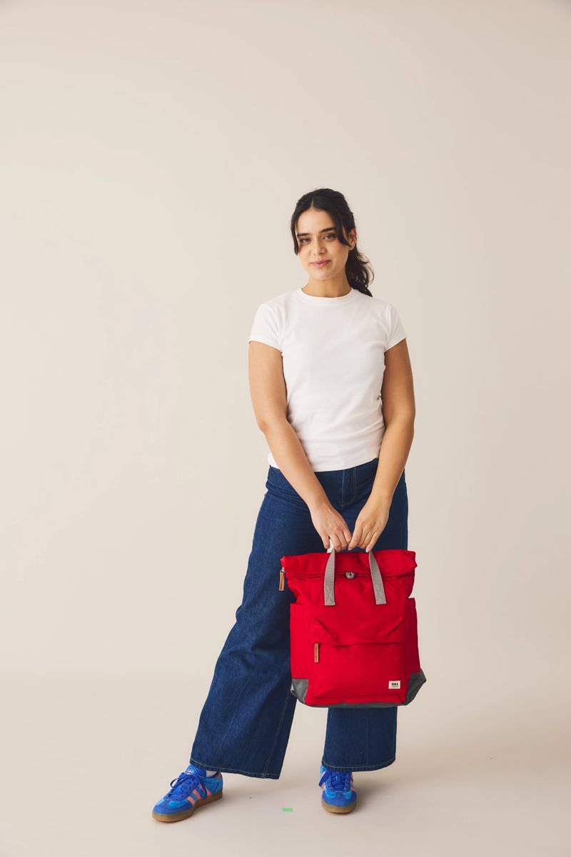 Model holding ROKA London Bayswater umbrella backpack in cranberry, with roll-top design and spacious front pocket