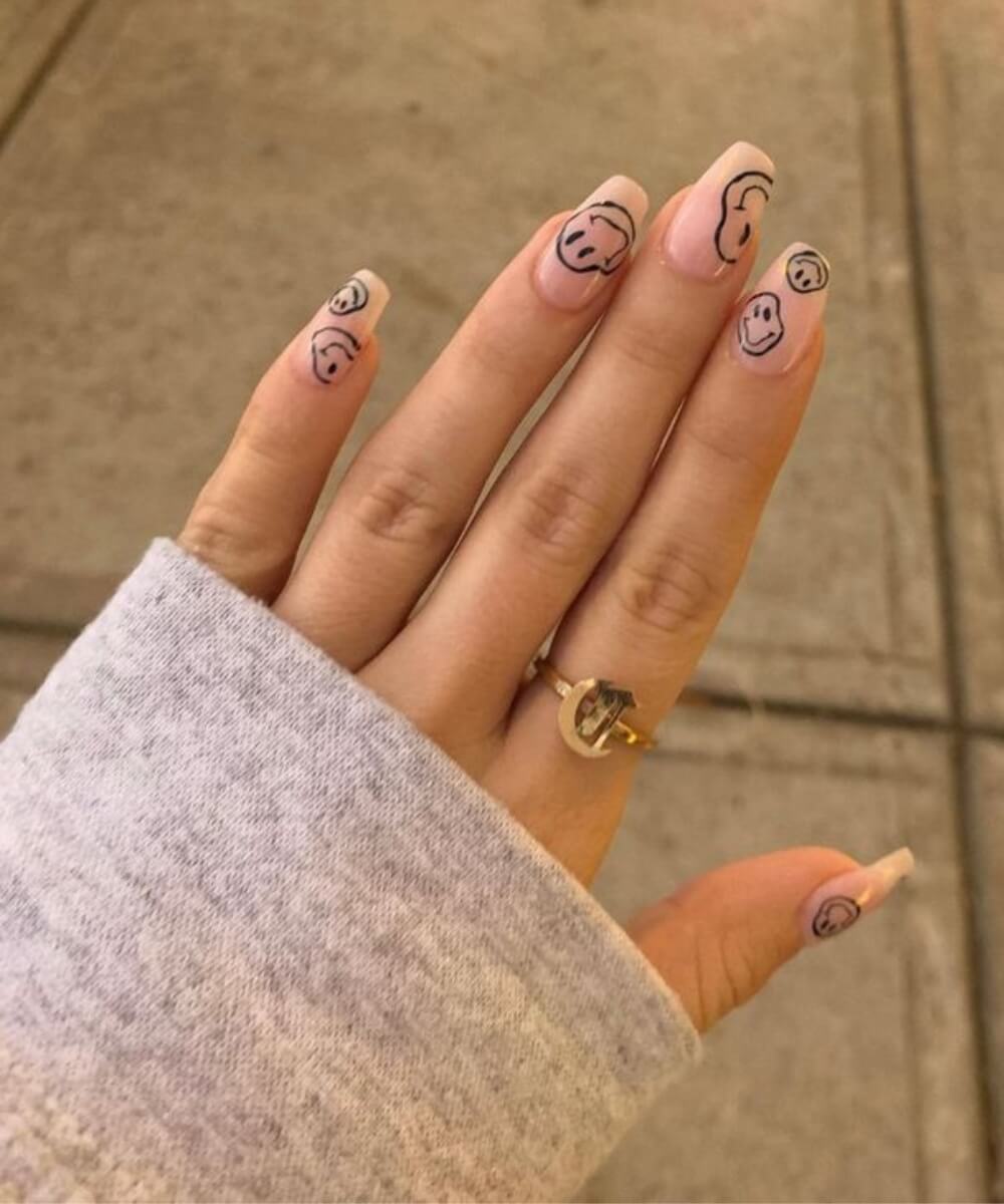 Close-up of almond-shaped nails with a sheer nude base, featuring simple black smiley face nail art and subtle French tips for a playful spring manicure