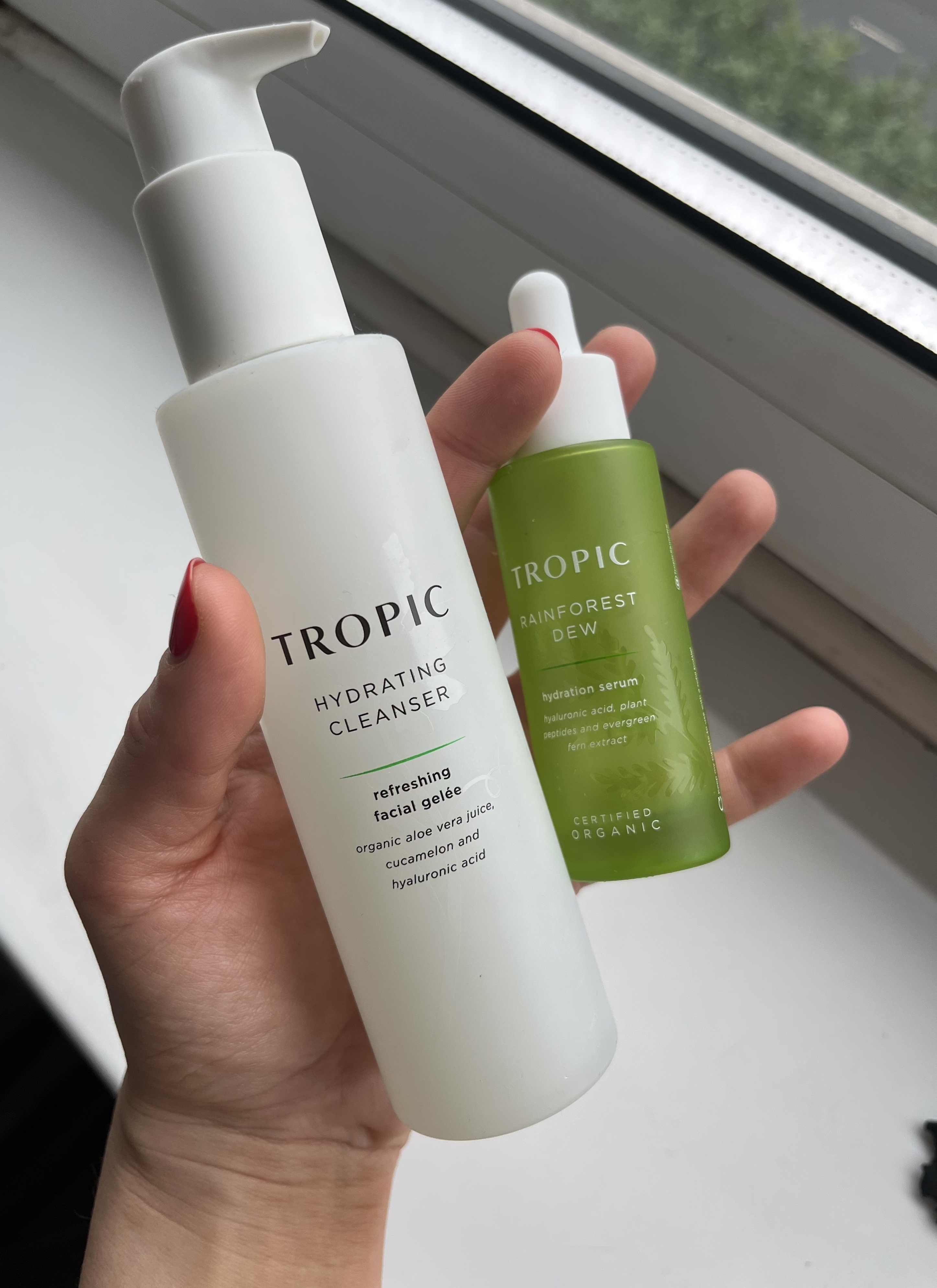 A woman's hand holding two empty Tropic skincare products, one of which is the Tropic Hydrating Cleanser and other is Tropic Rainforest Dew Hydration Serum which helped with adult acne