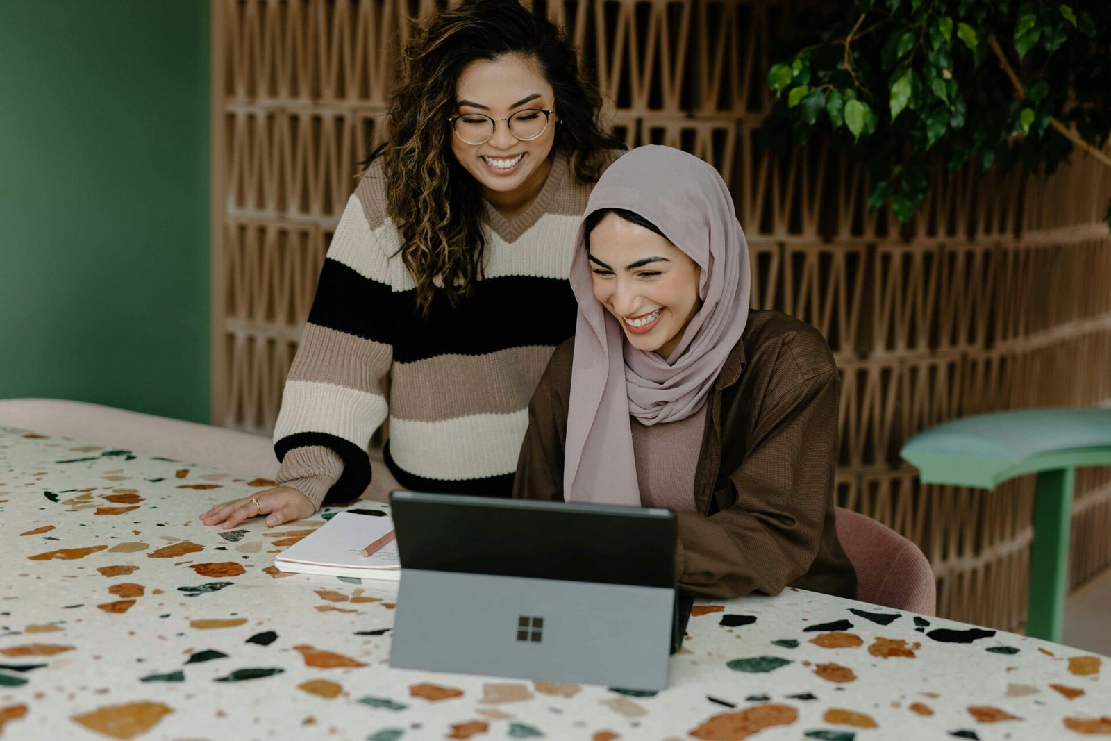 Two female founders stand and sit at a table, focused on a laptop, engaged in discussion or collaboration representing the idea of investors