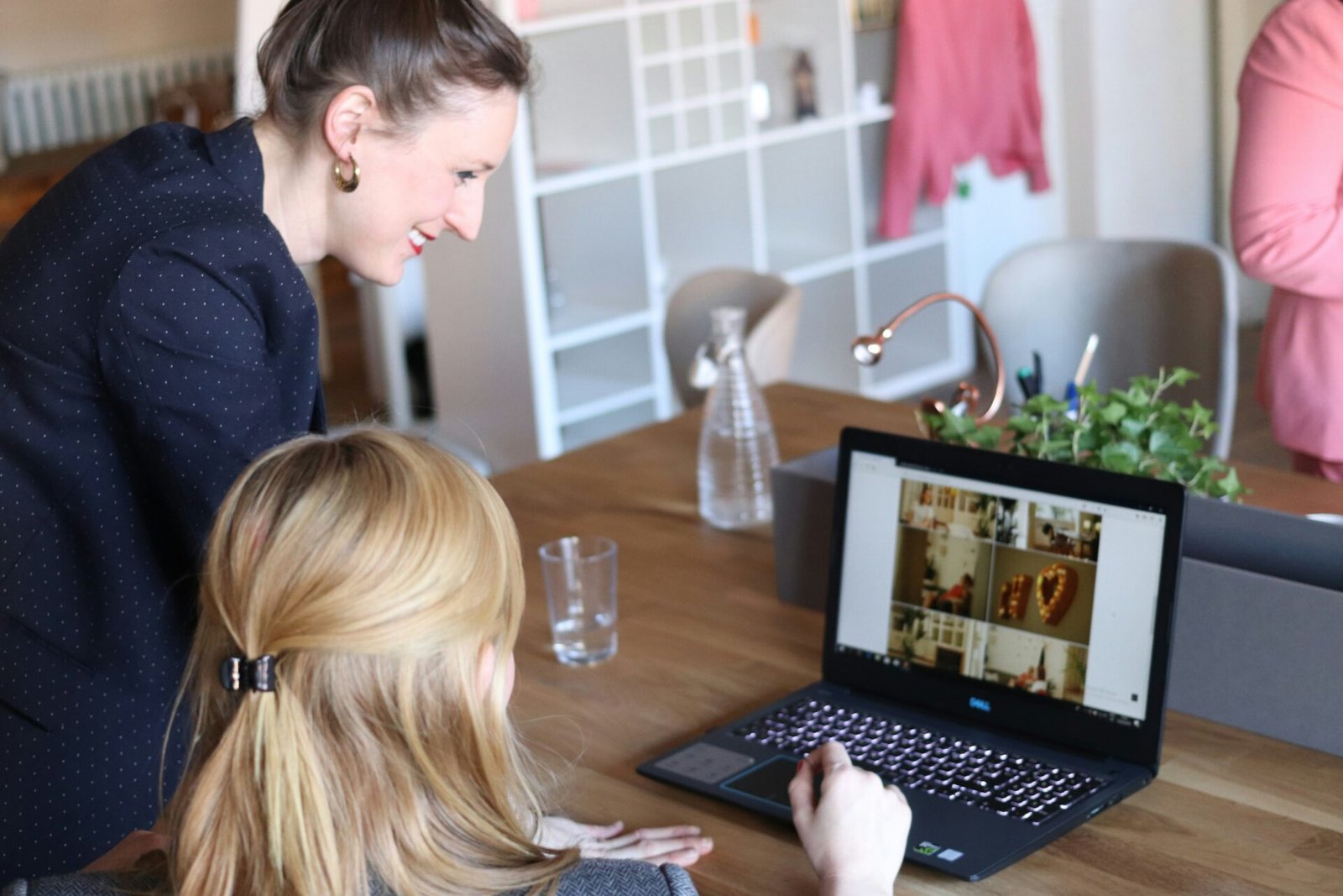 A woman gazes at a laptop screen while another woman sits at a table, engaged in conversation - best investors for female founders