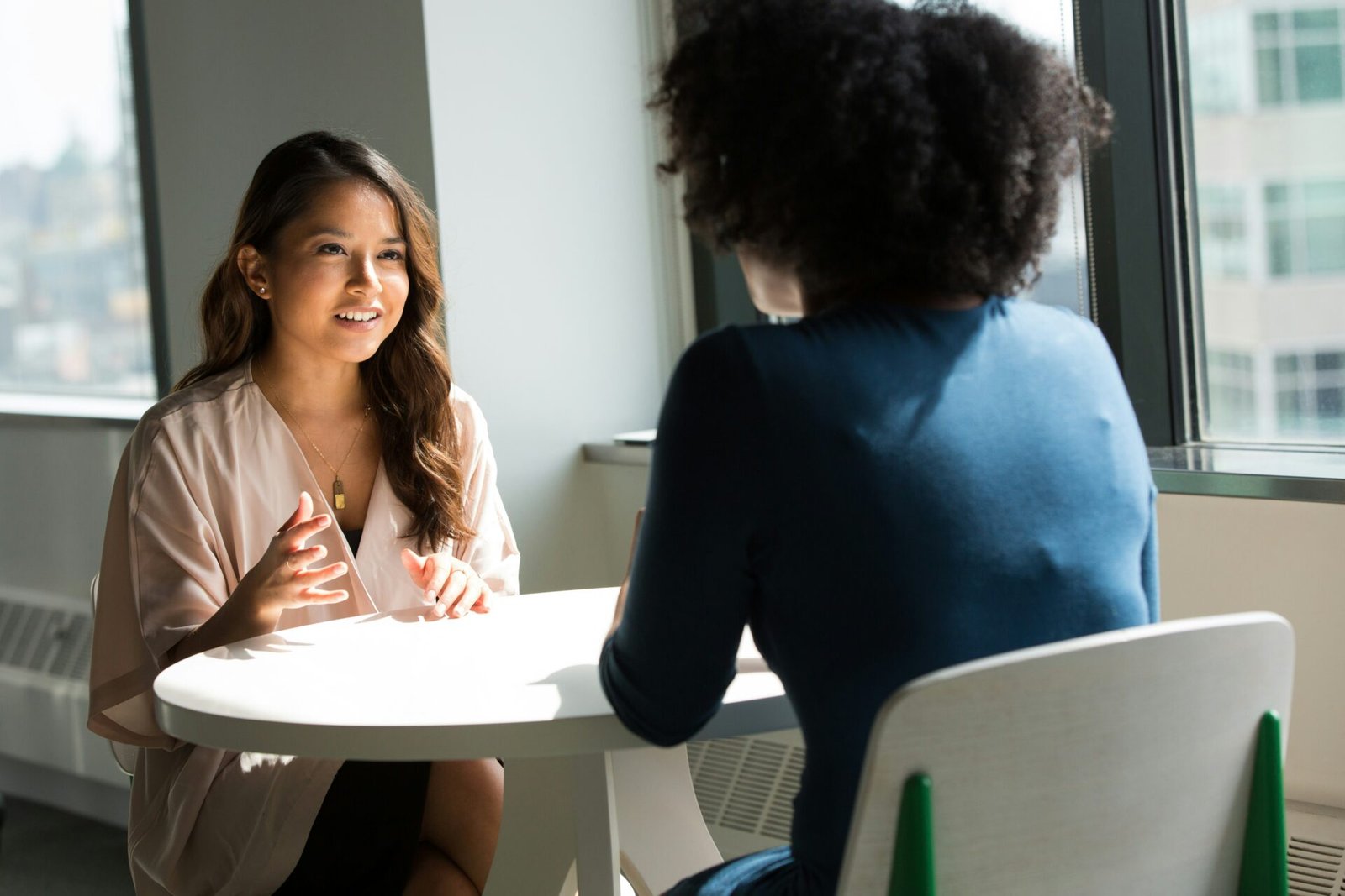Two women at a business meeting converse at a table, with one woman actively speaking while the other listens intently - best investors for women-led businesses