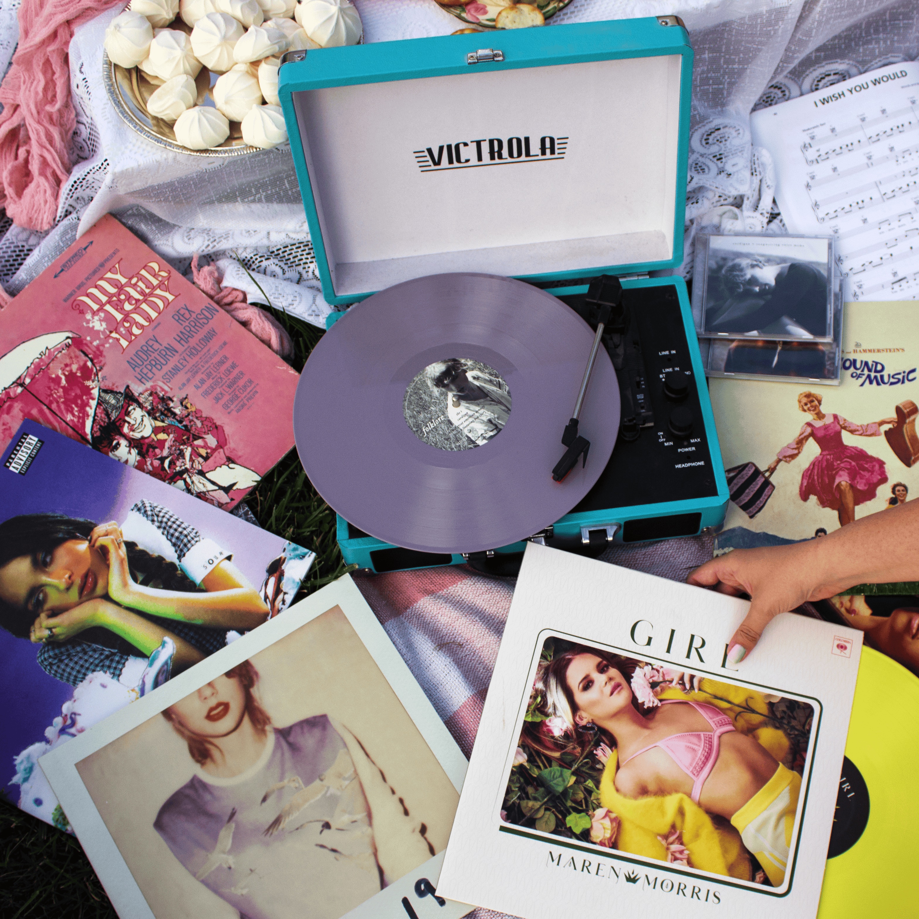 Victrola record player playing a vinyl record surrounded by albums including Maren Morris 'Girl', Taylor Swift and Sound of Music musical soundtrack records - Best Girl Power Songs of All Time.