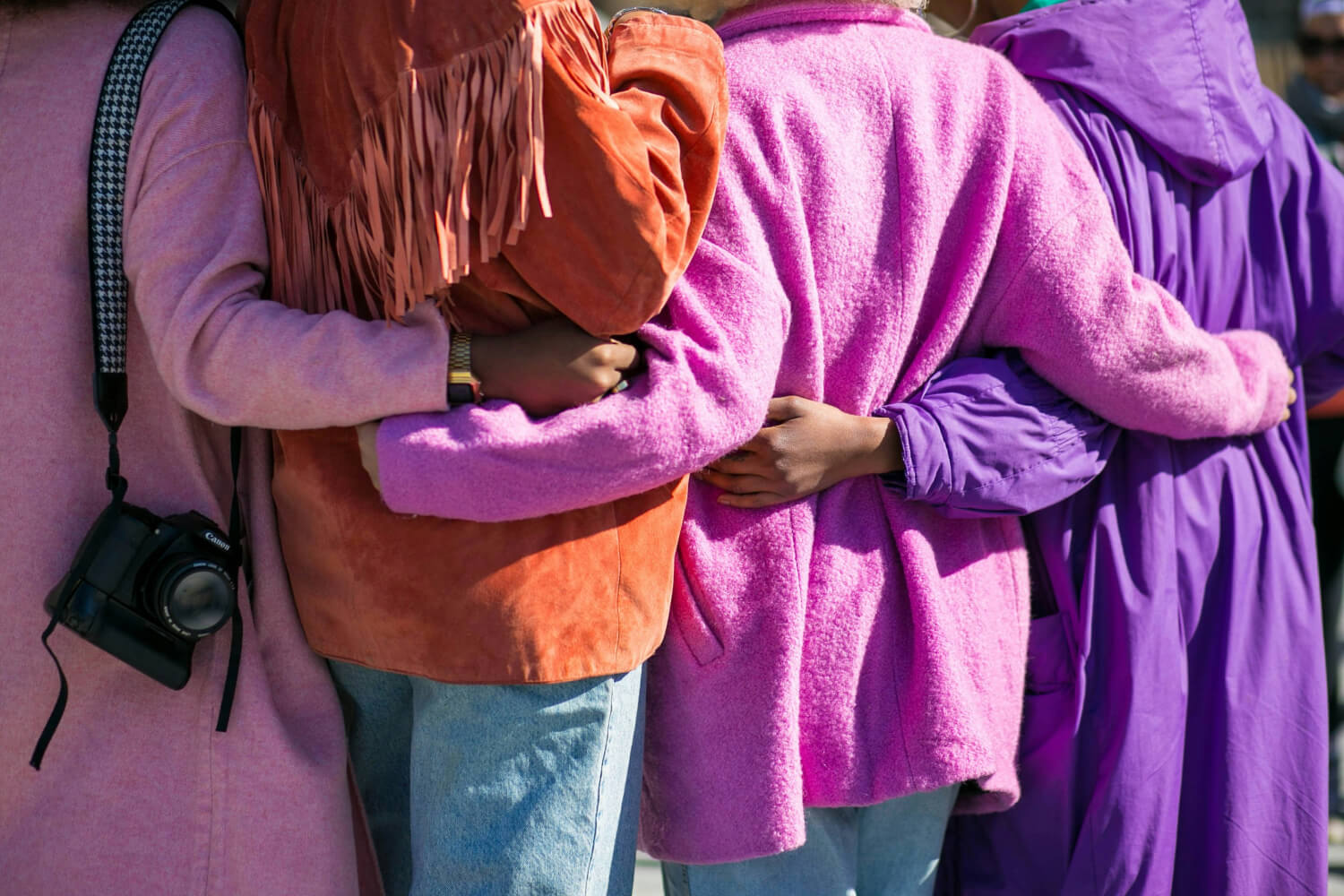 Four women standing together, wearing colourful jackets and holding each other warmly