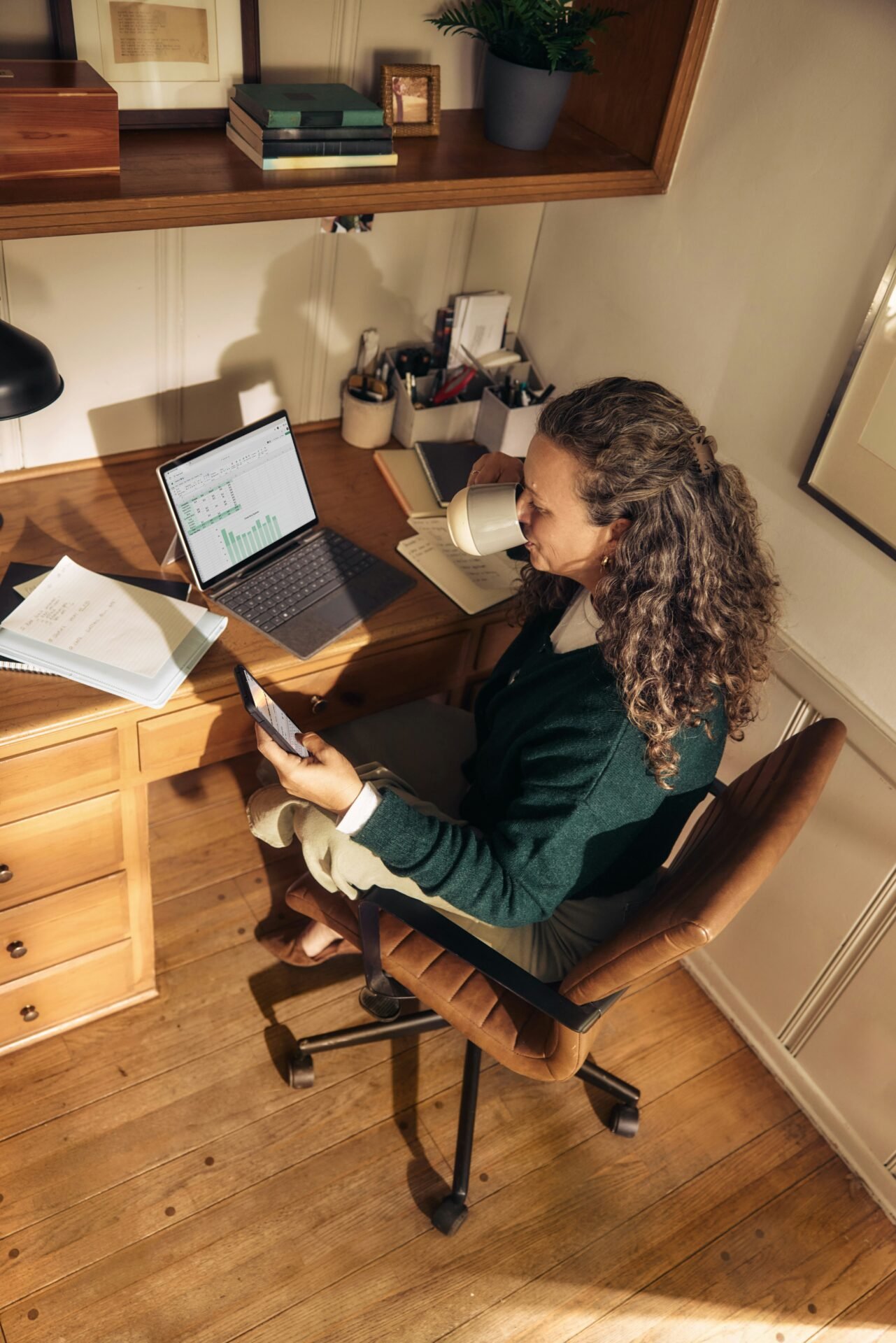 A woman seated at a desk, working on a laptop with a cup of coffee beside her