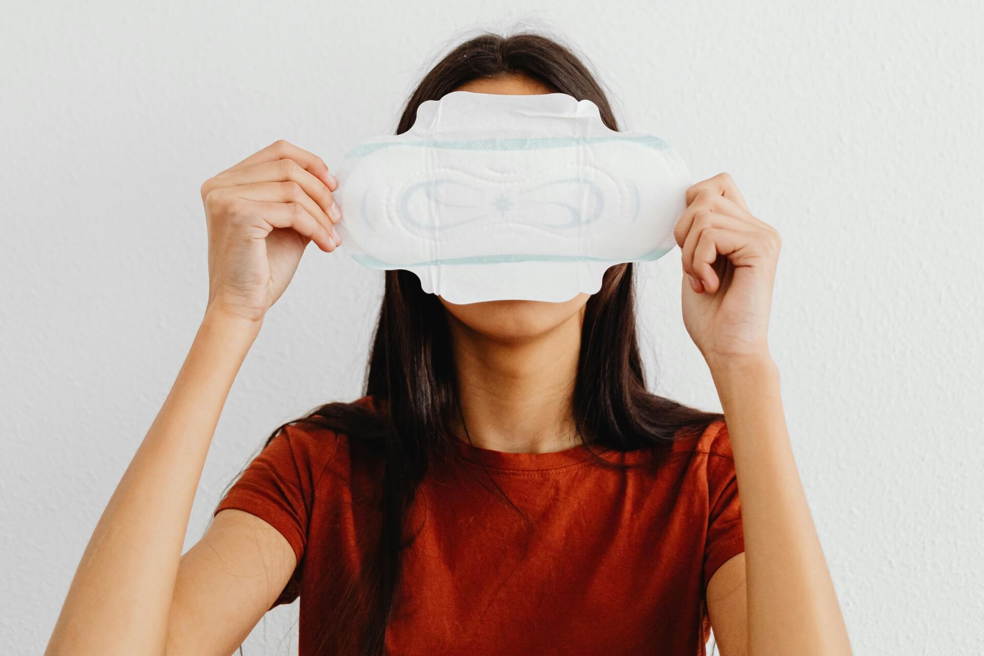 A woman holds a sanitary pad in front of her face against a plain background, highlighting menstrual health taboos and free period product awareness
